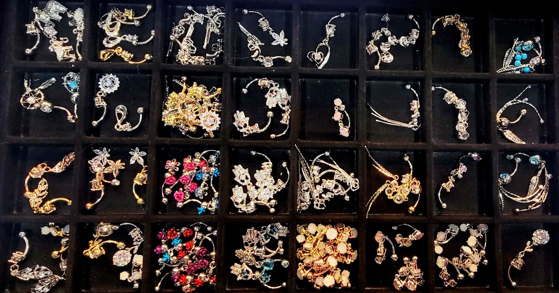 Jewelry display: earrings with various floral and abstract designs, silver and gold, with colorful gems.