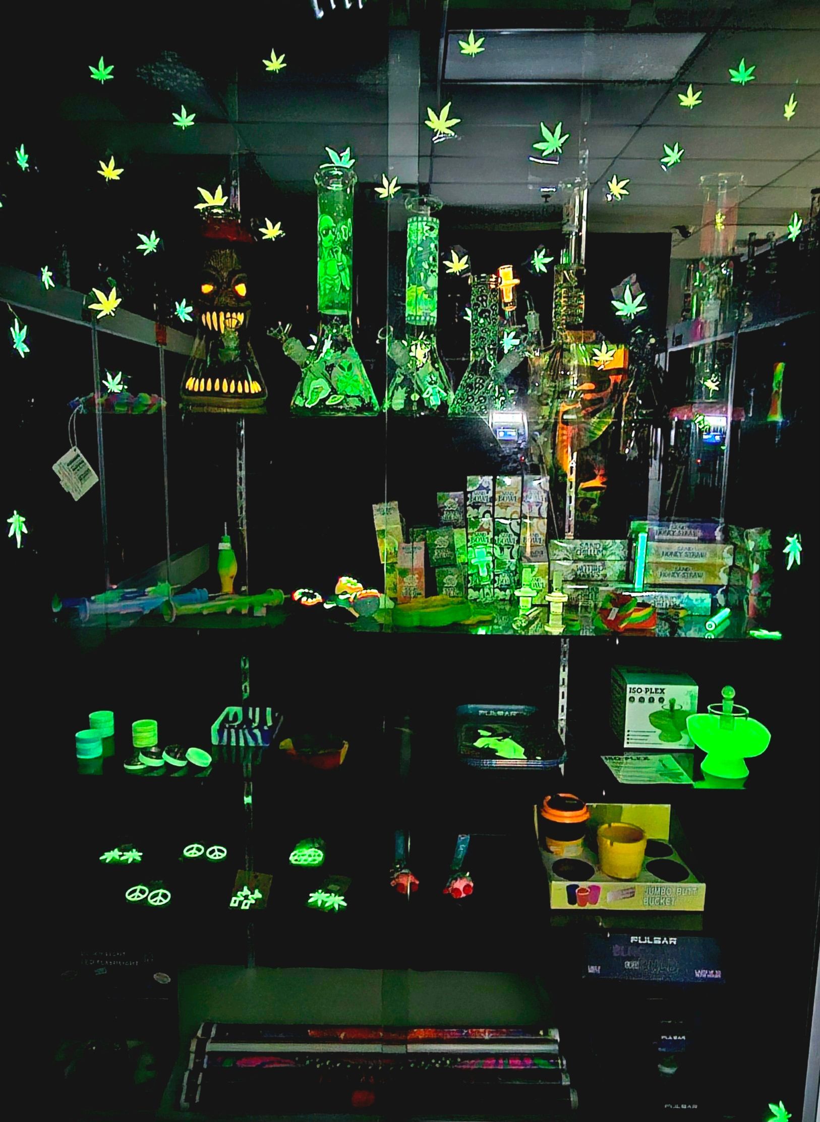 Glow-in-the-dark display of glass bongs and accessories inside a store, with neon green accents.