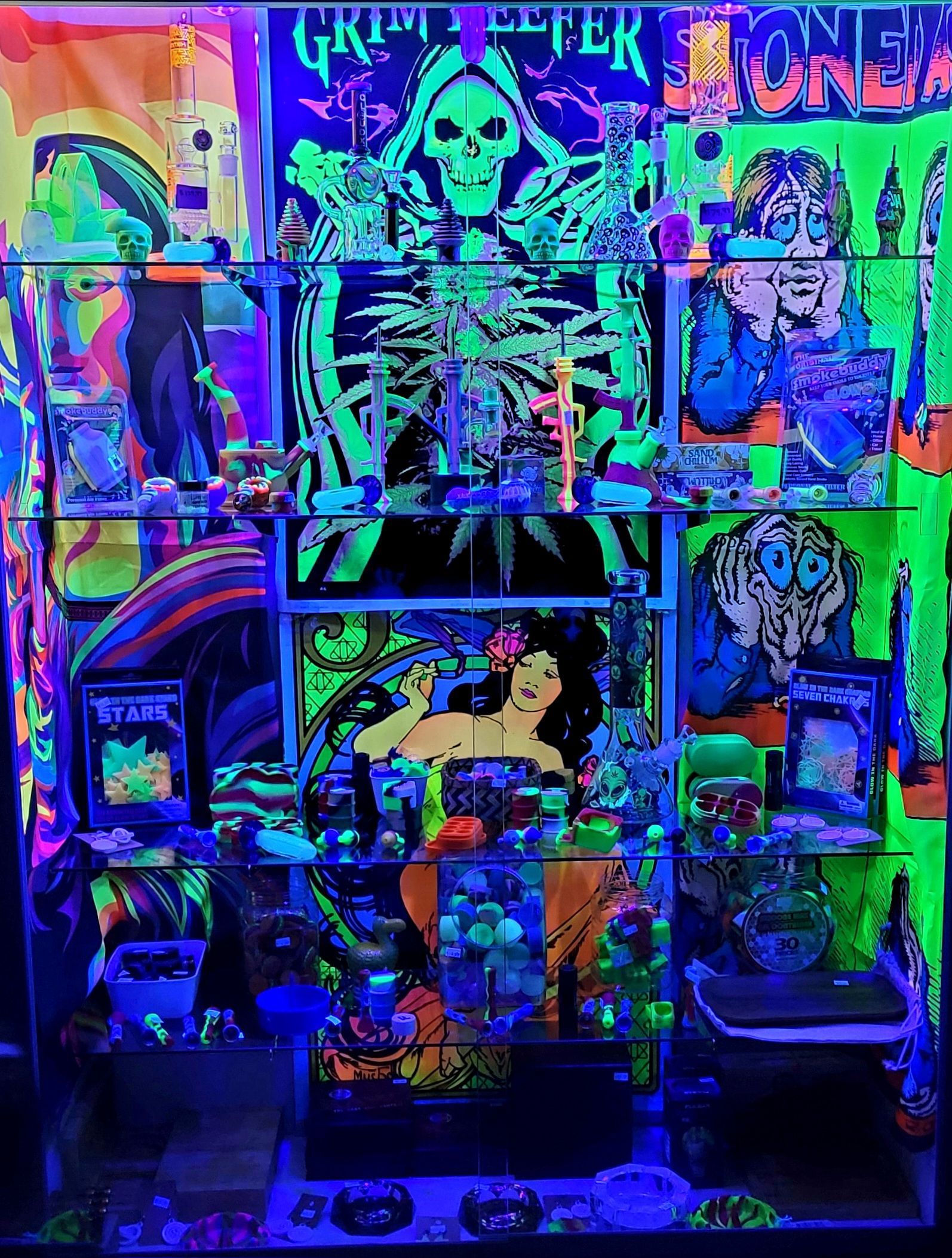 Blacklight display of posters, figurines, and objects, glowing neon green and blue. Skeletal figure and psychedelic art.