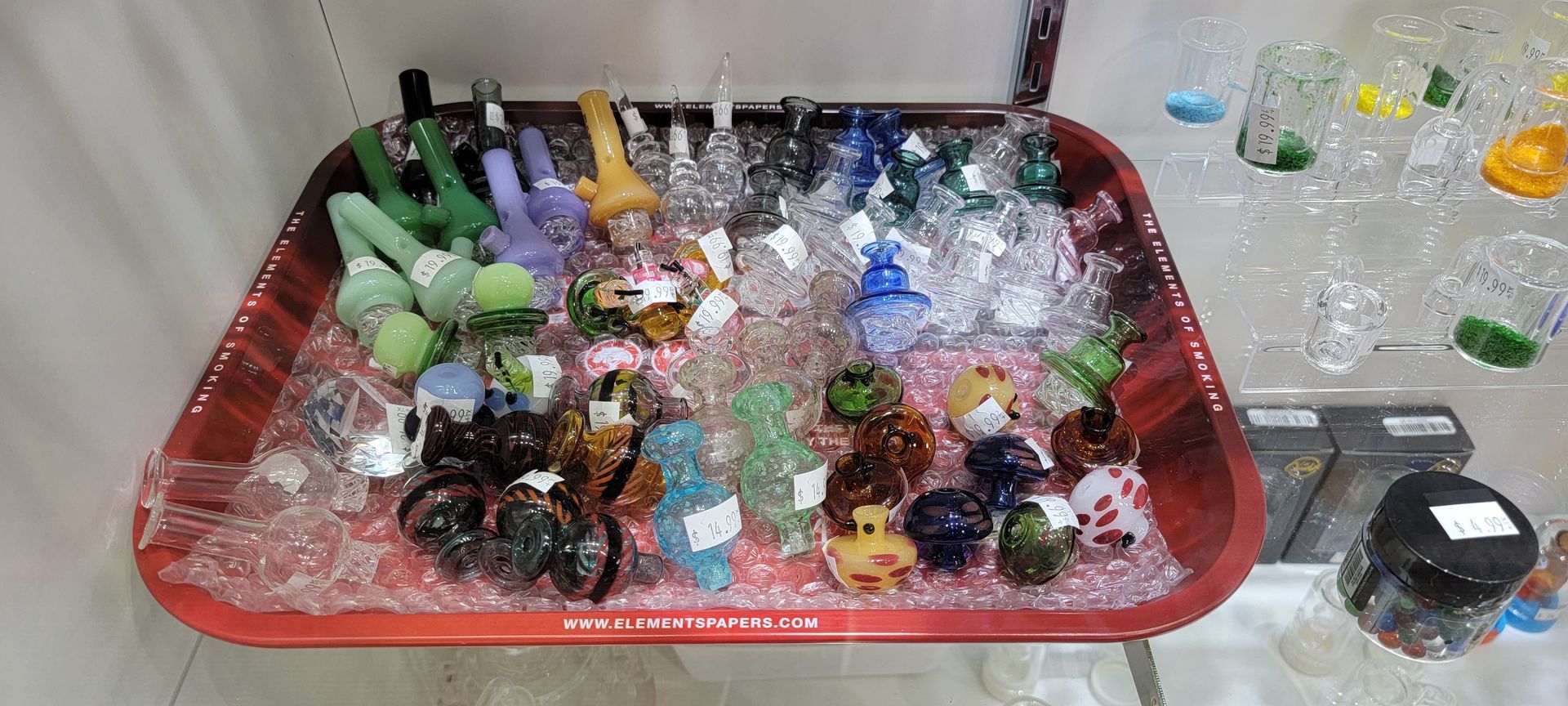 A red tray filled with various colorful glass smoking pipes, in a store setting.