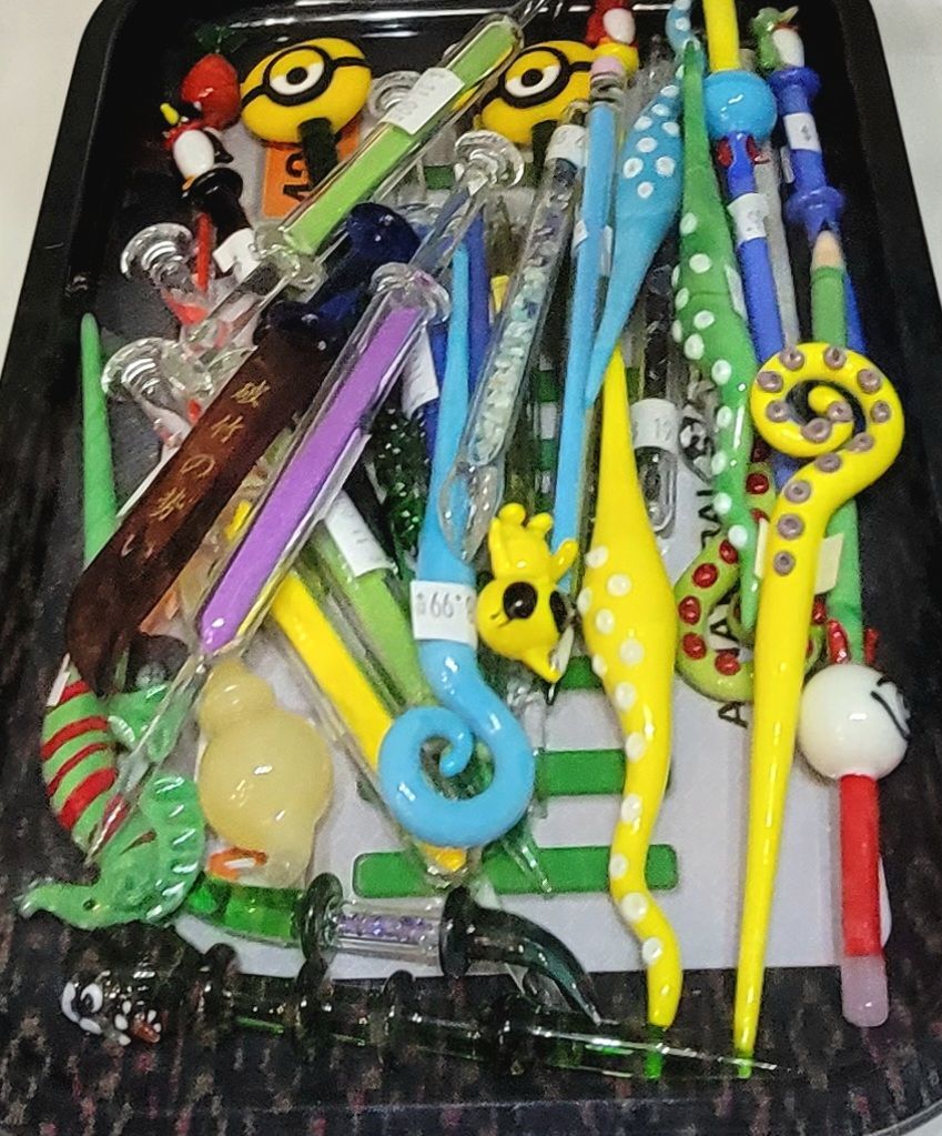 Tray of colorful, decorative glass dab tools in various shapes: Minions, seahorses, and others.