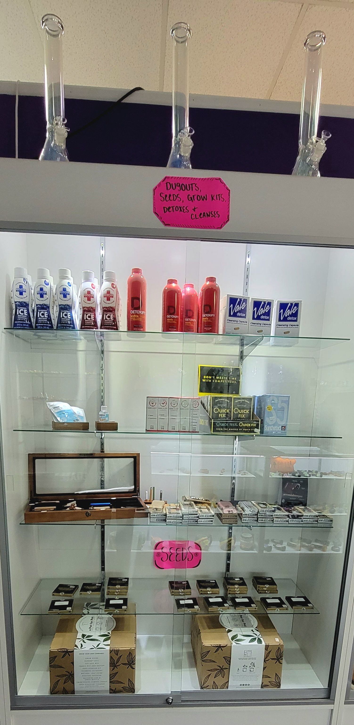 A glass display case in a shop with bongs at the top. Shelves display various items like cleaning solutions and boxes.