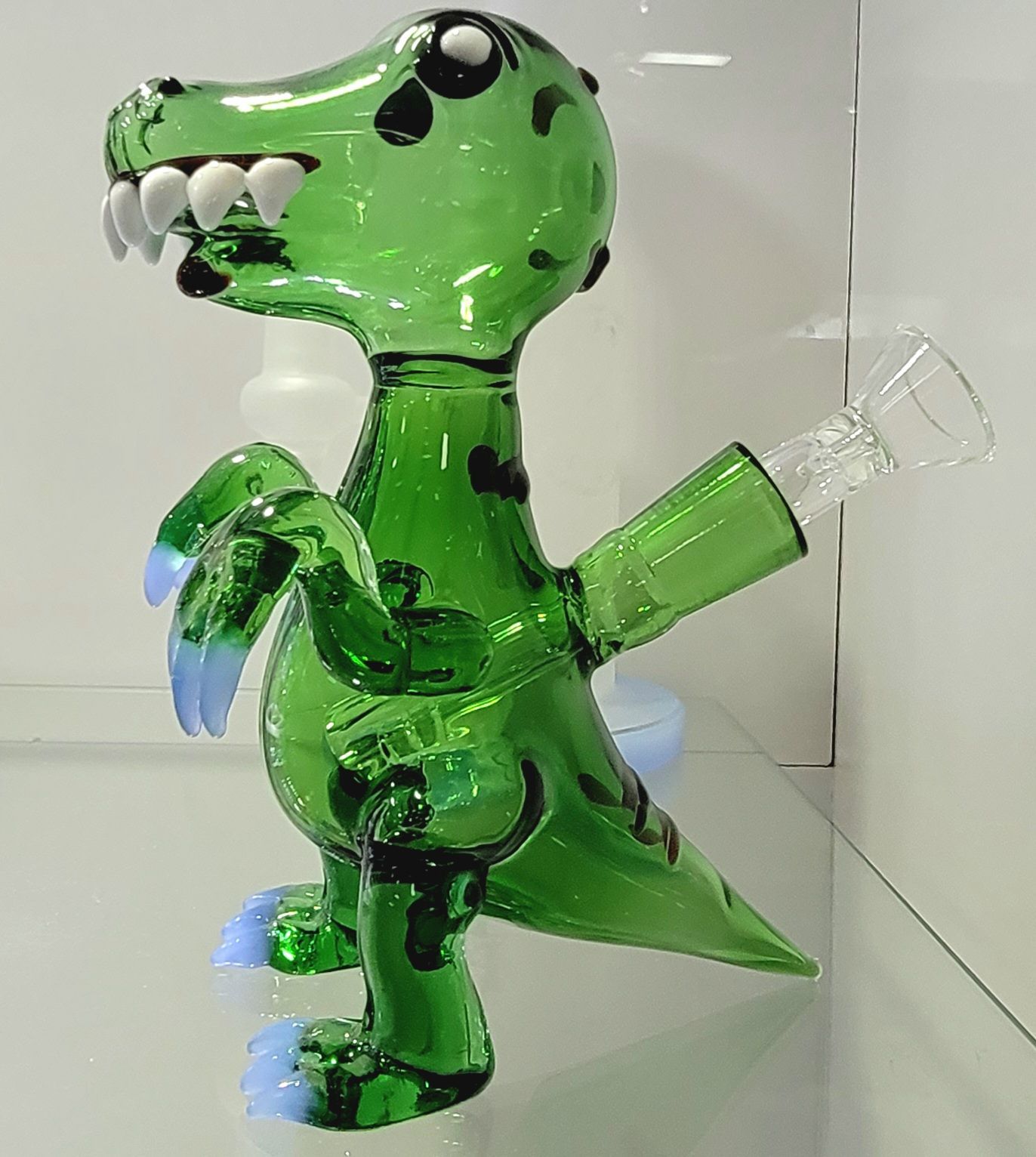 Green glass dinosaur bong with white teeth, black spots, and blue accents, on display.