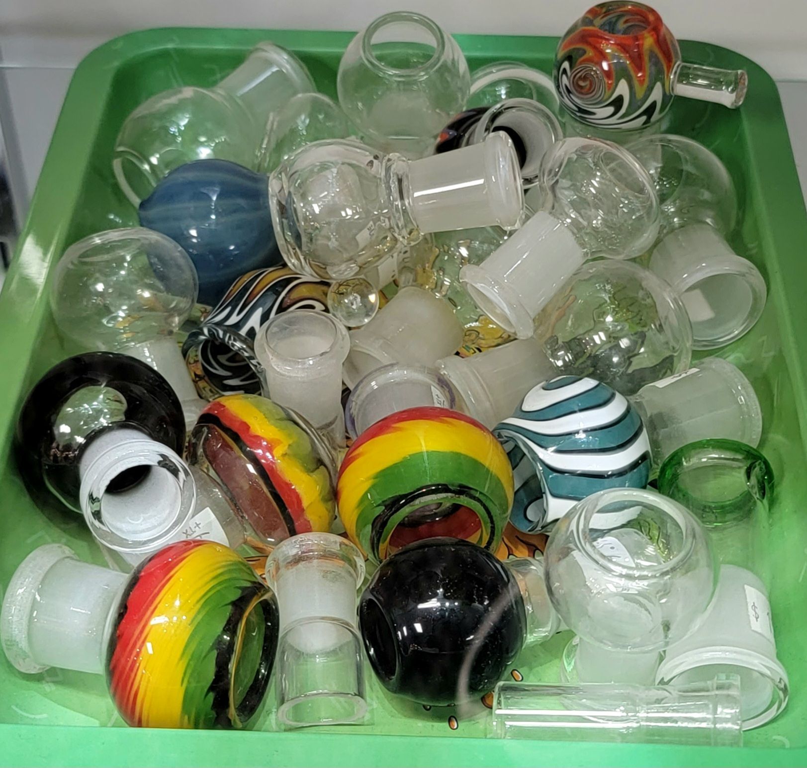 A green bin filled with various glass bong bowls and accessories of different colors and designs.
