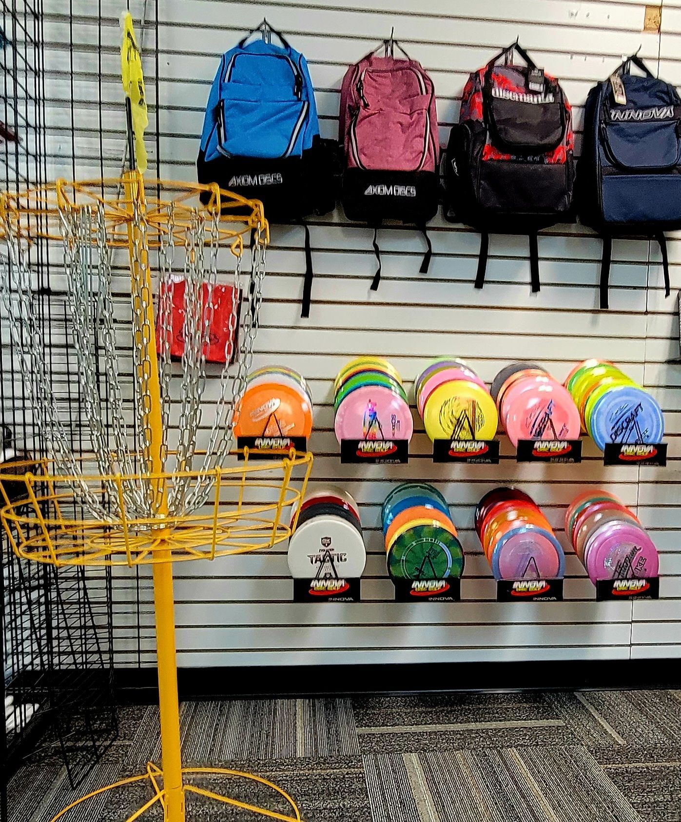 Yellow disc golf basket in front of a display of disc golf bags and discs.
