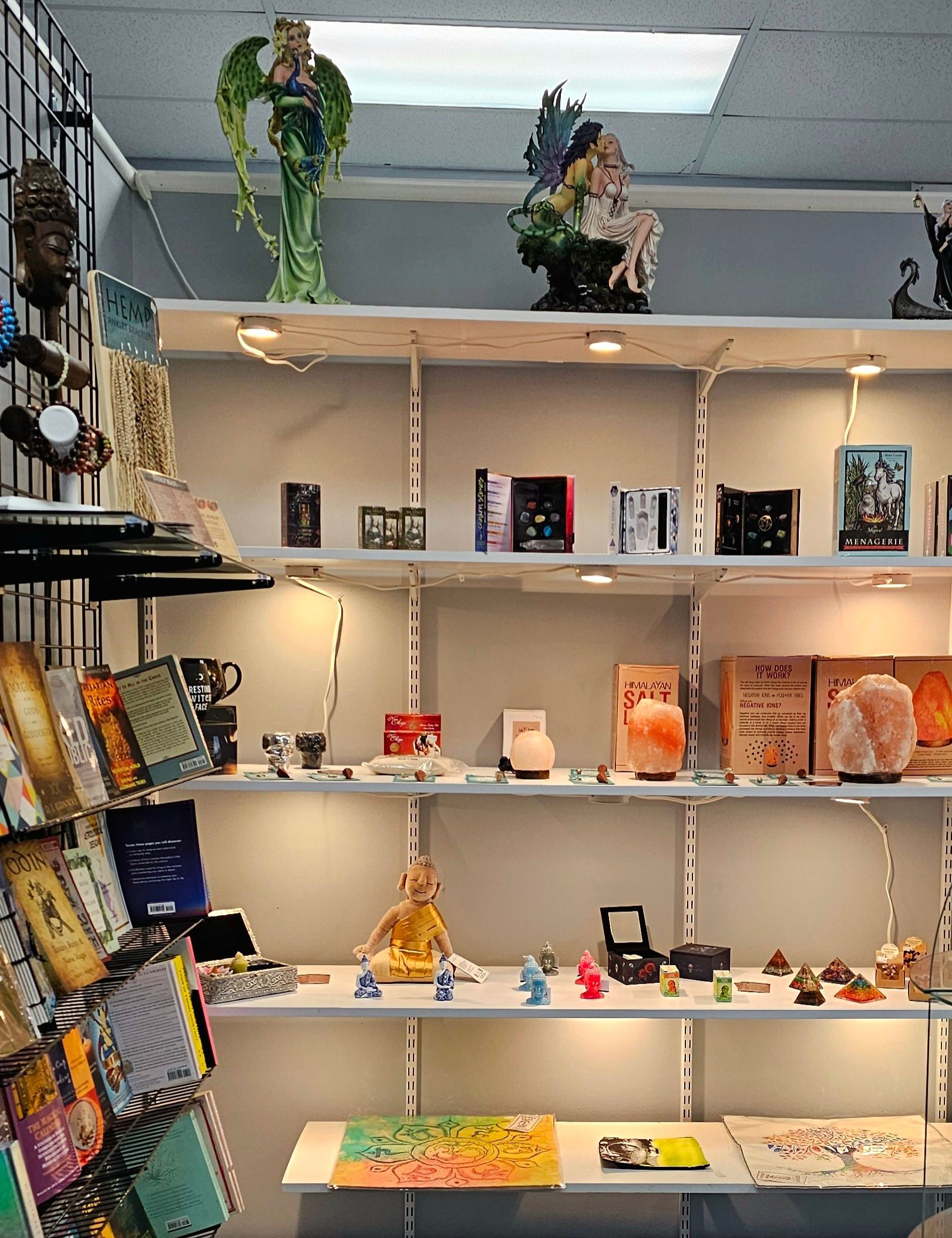 Shelves display various spiritual items, including statues, books, and crystals. Well-lit shop interior.