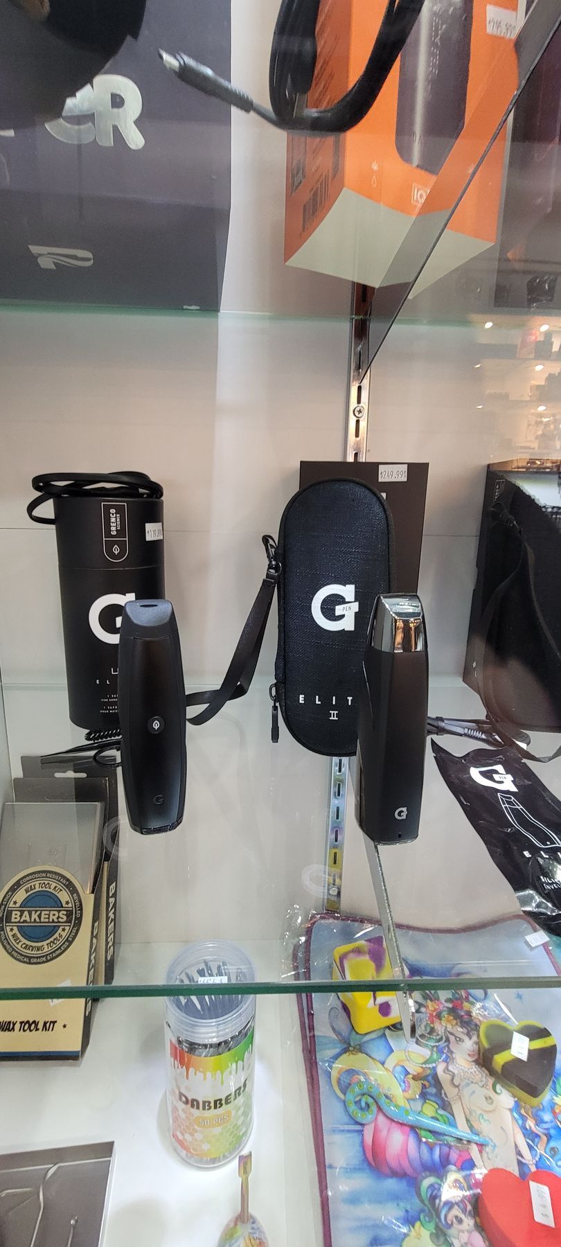 Display case with black vape accessories, including a carrying case with a strap and a tall cylindrical case.