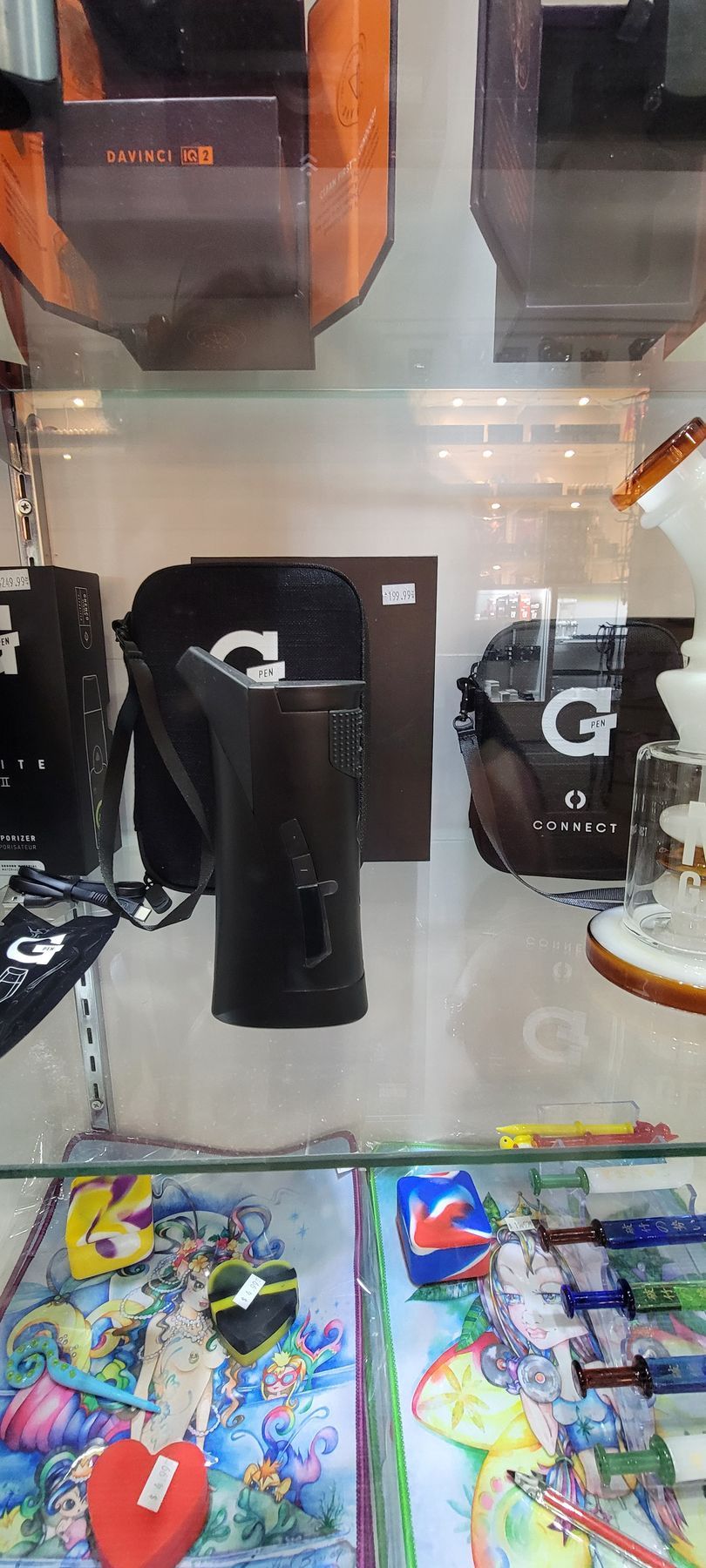 A black vaporizer sits inside a glass display case with other smoking accessories.