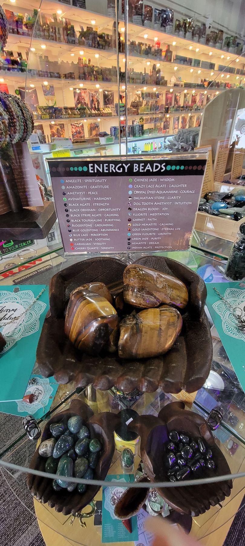 Display case with gemstones, including tiger's eye, green and black stones, against a backdrop of shelves with items.