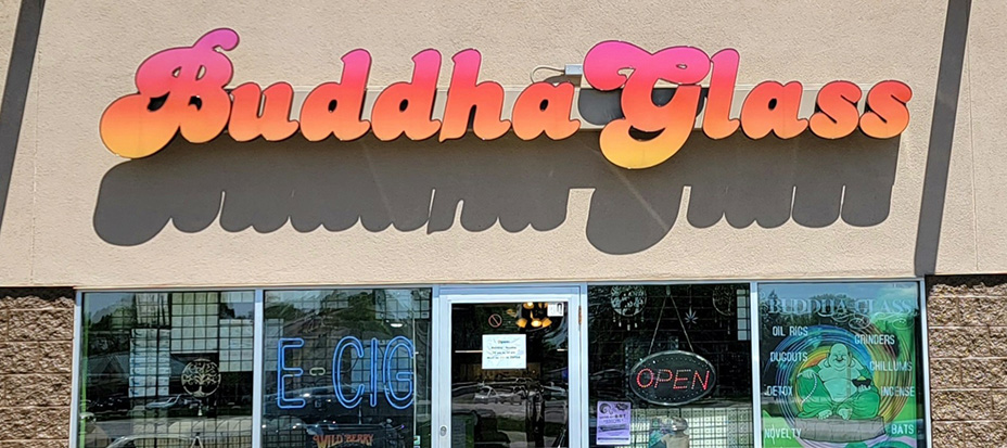 Buddha Glass store sign with a gradient from orange to pink.  Below is a storefront with a sign that says, 