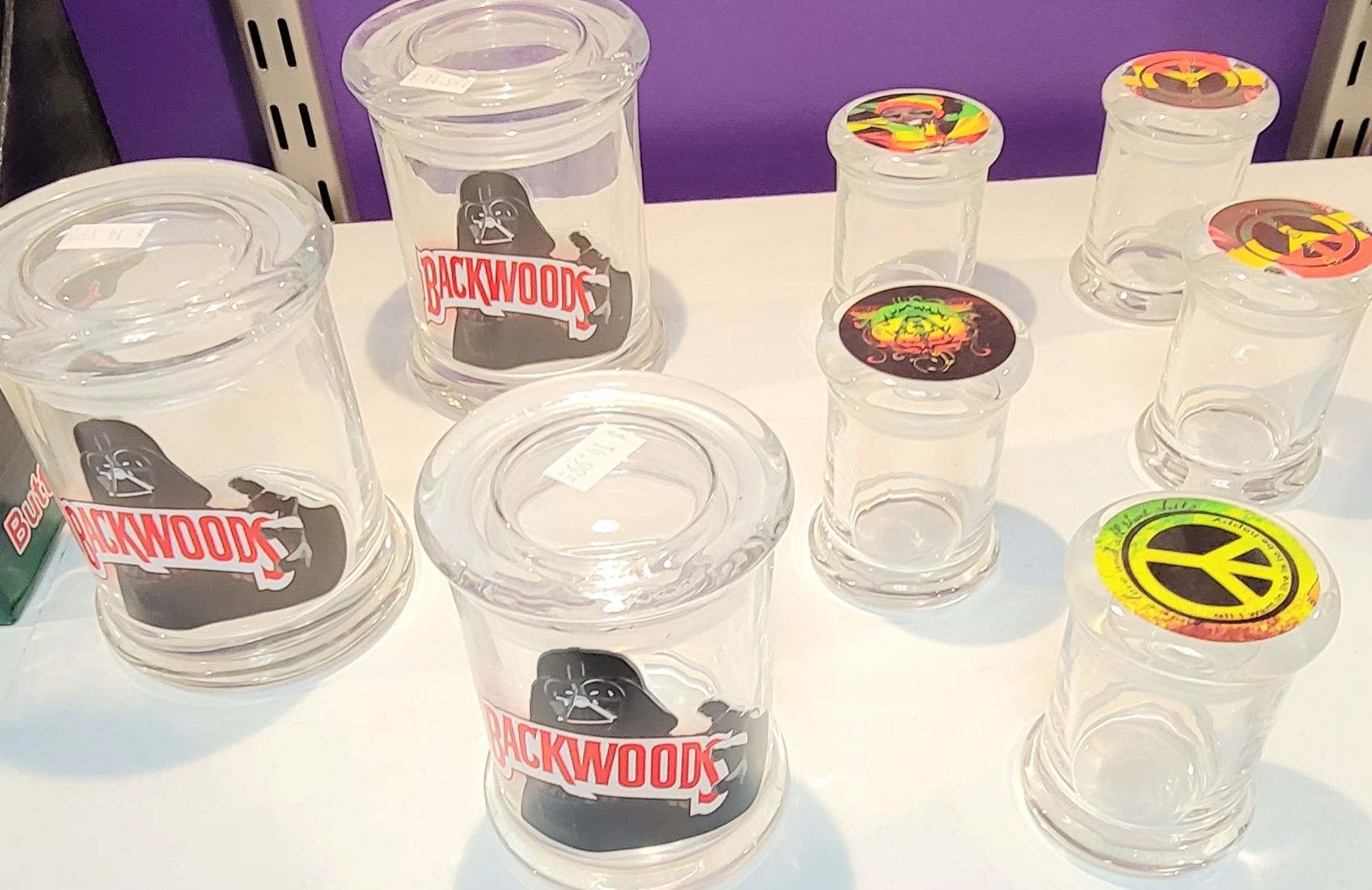 Clear glass jars on a table, some with logos and colorful lids, possibly for storage.