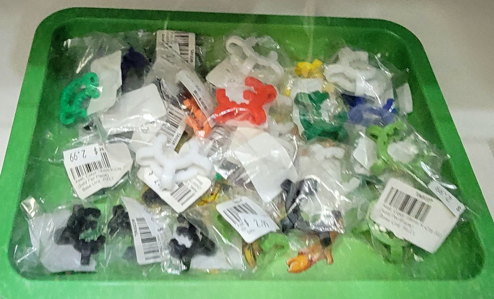 A green tray filled with numerous small, plastic toys in clear plastic bags, various colors, and tags attached.