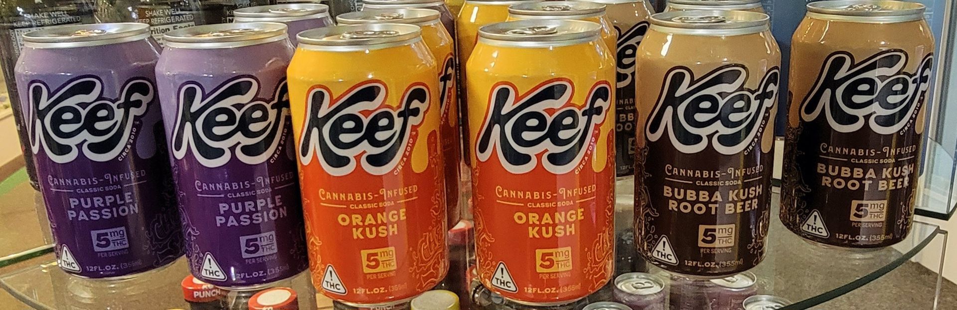 Row of Keef cannabis-infused soda cans, featuring purple, orange, and brown flavors.