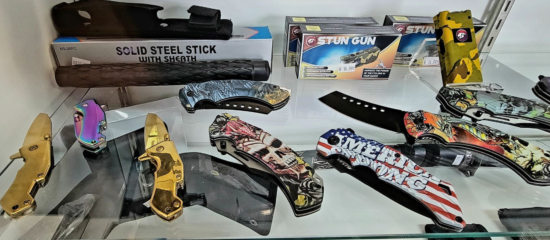 Display of various pocket knives with decorative handles, on shelves in a store.