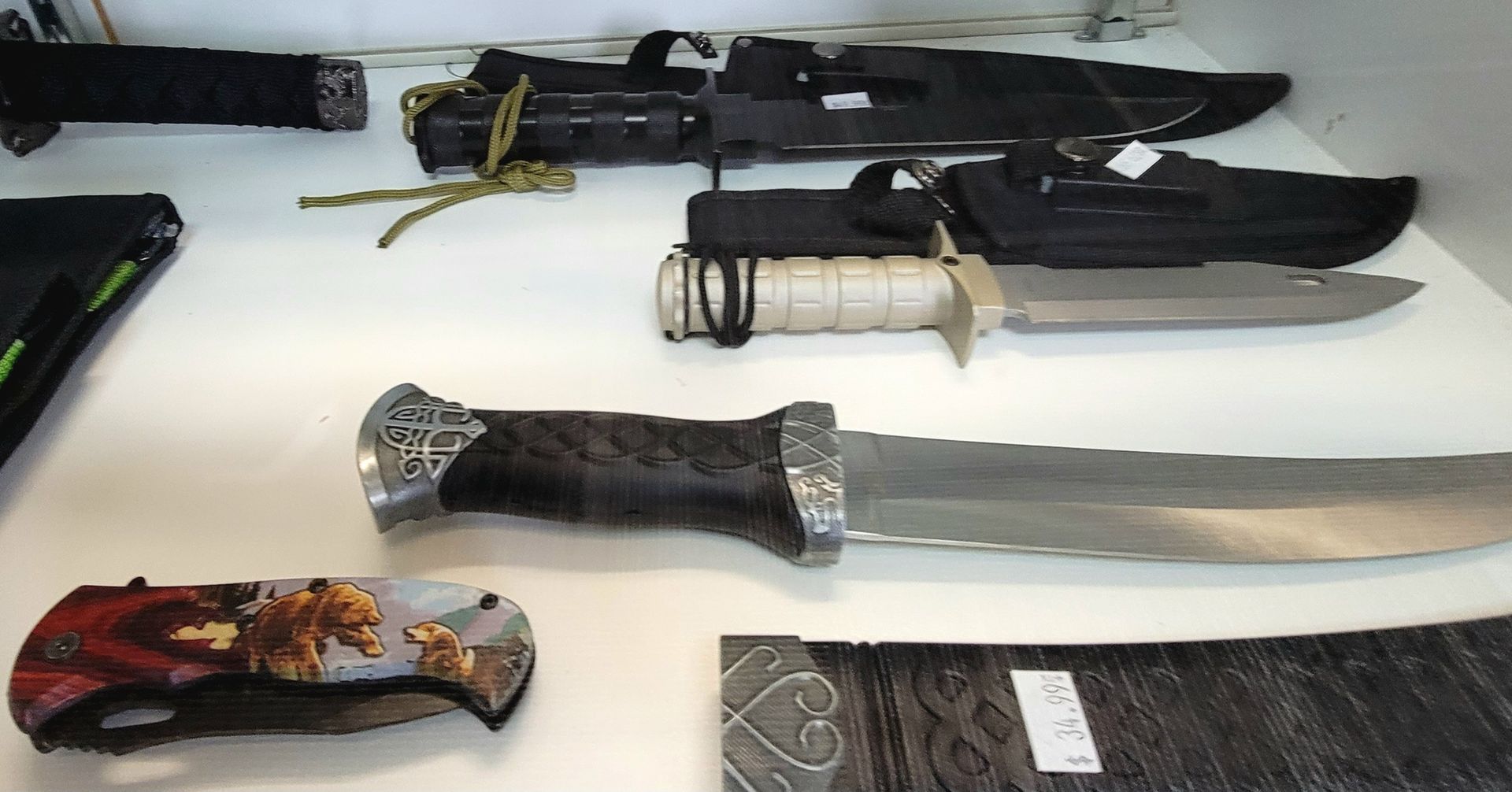 Knives displayed on a shelf, including a folding knife with a bear design and larger knives with sheaths.