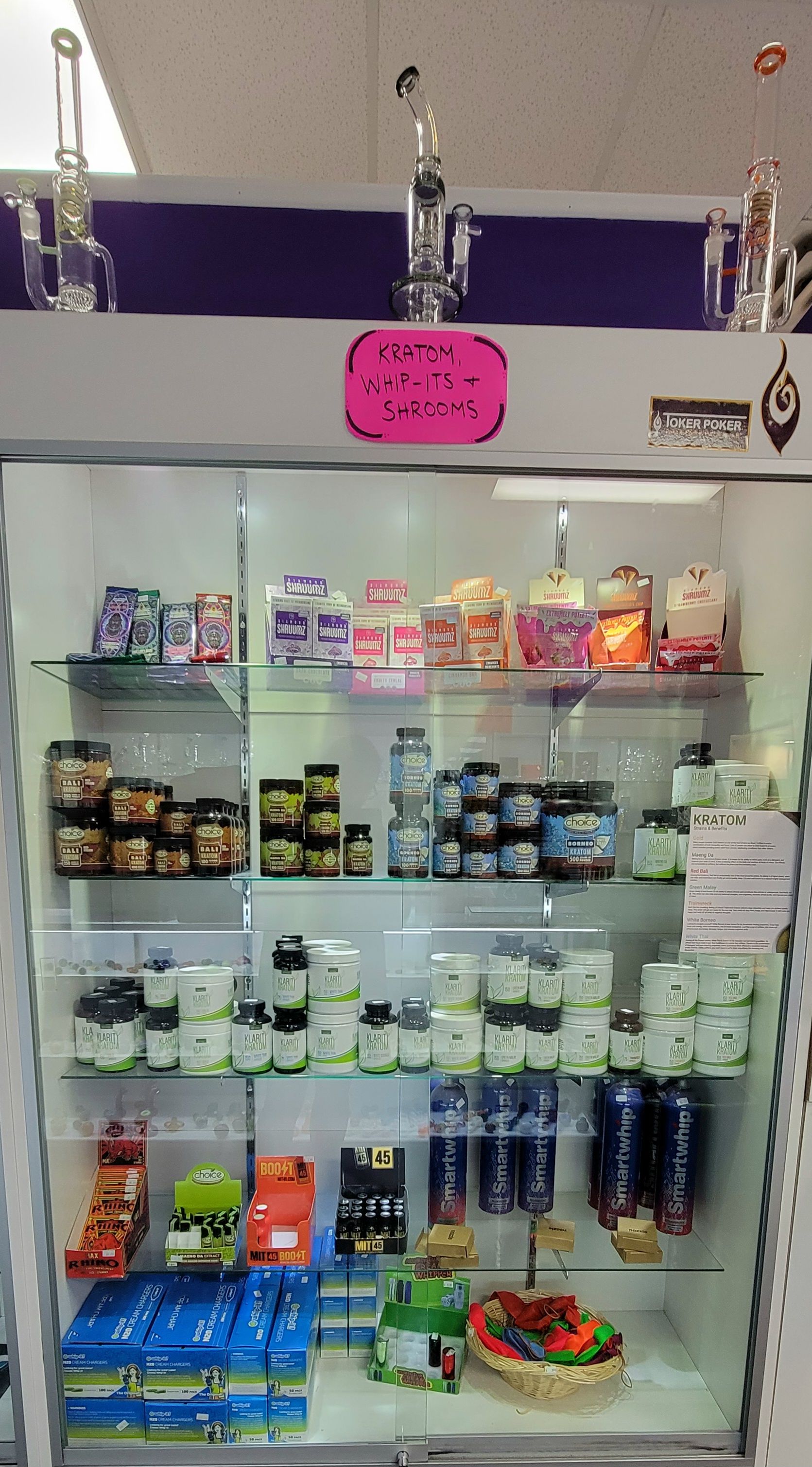 Glass display case filled with packaged supplements and some glass bongs, inside a store.