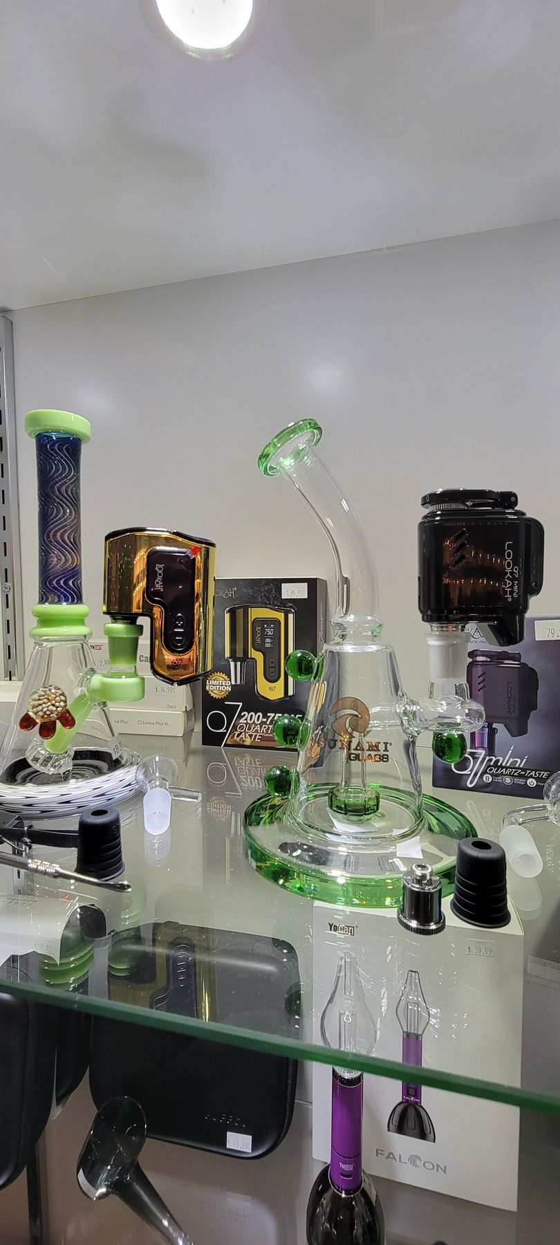 Display of glass smoking devices in a shop. Glass bongs and vaping equipment sit on a glass shelf.