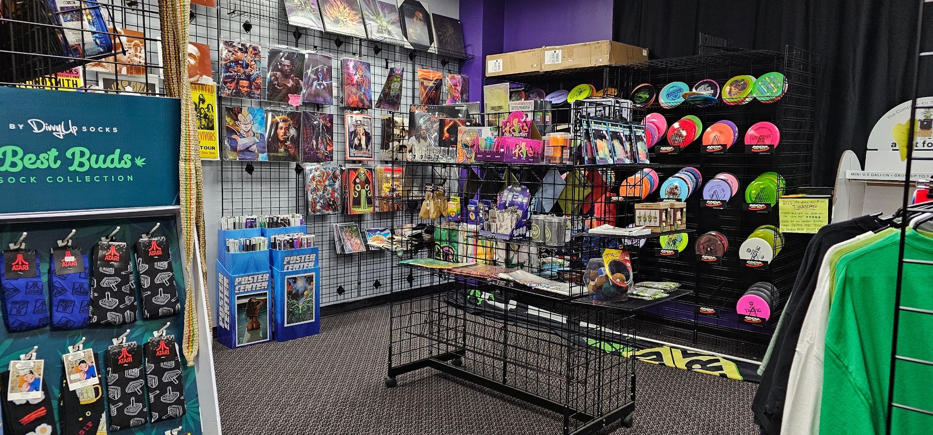 Inside of a store, displays merchandise. Racks of comics, hats, socks and t-shirts. Purple wall and black racks.