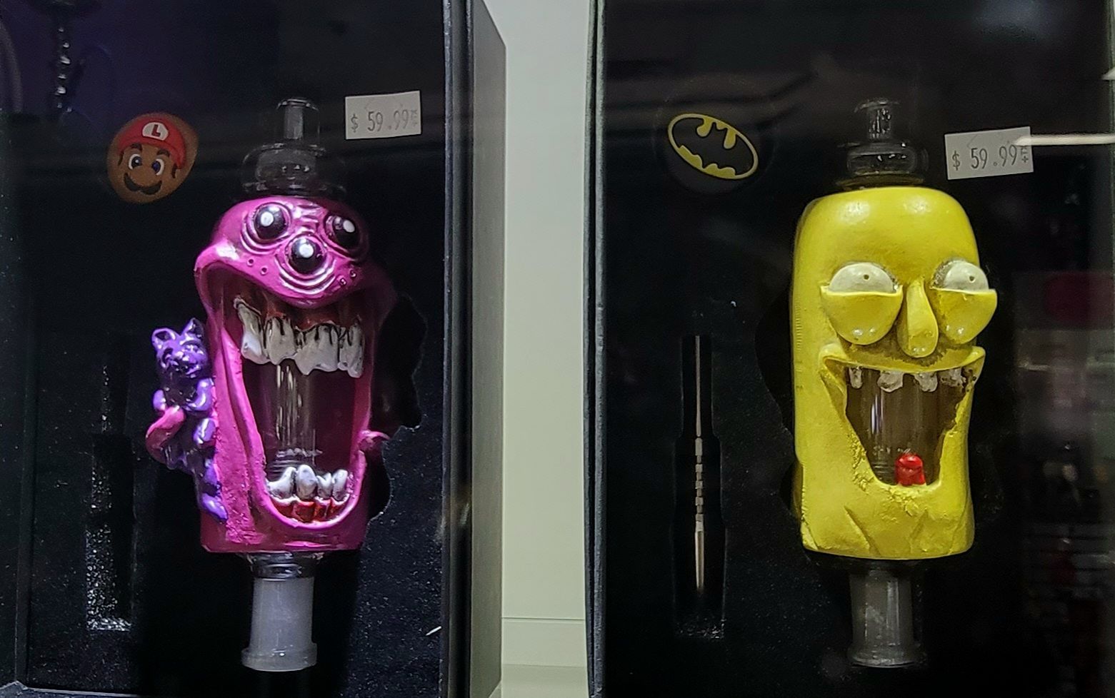 Two novelty bongs: a pink monster and a yellow Rick & Morty character, displayed in cases.