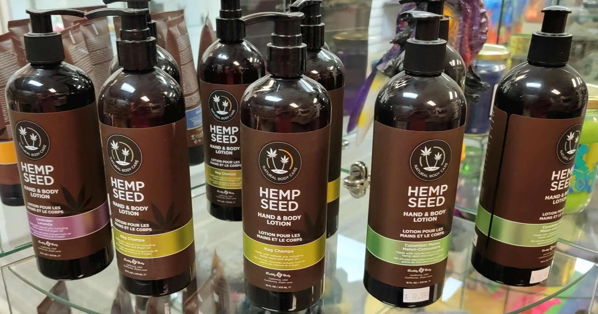 Bottles of hemp seed lotion with colored labels sit on a shelf.