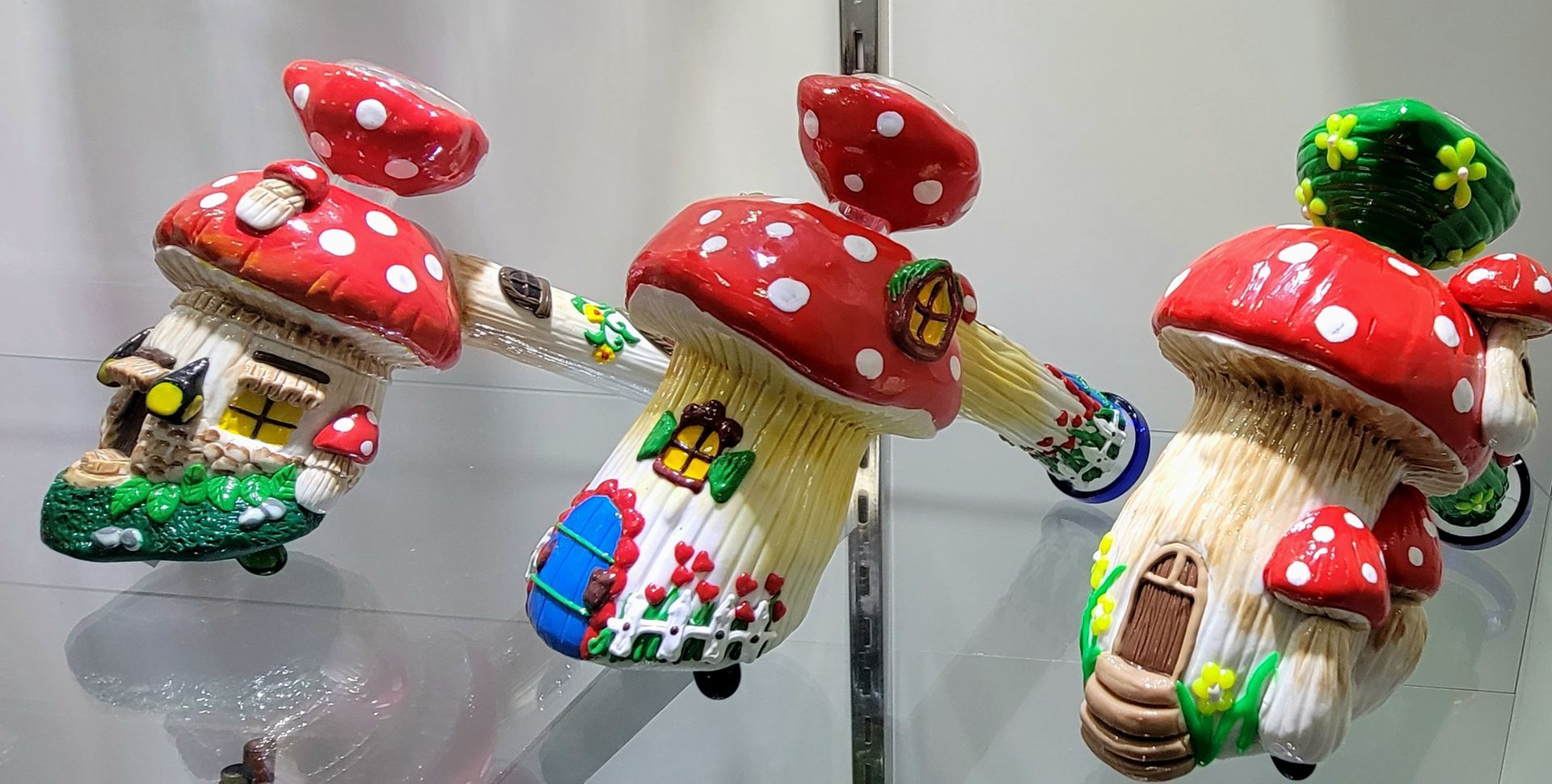 Three whimsical mushroom houses with red and white spotted caps, displayed on a shelf.