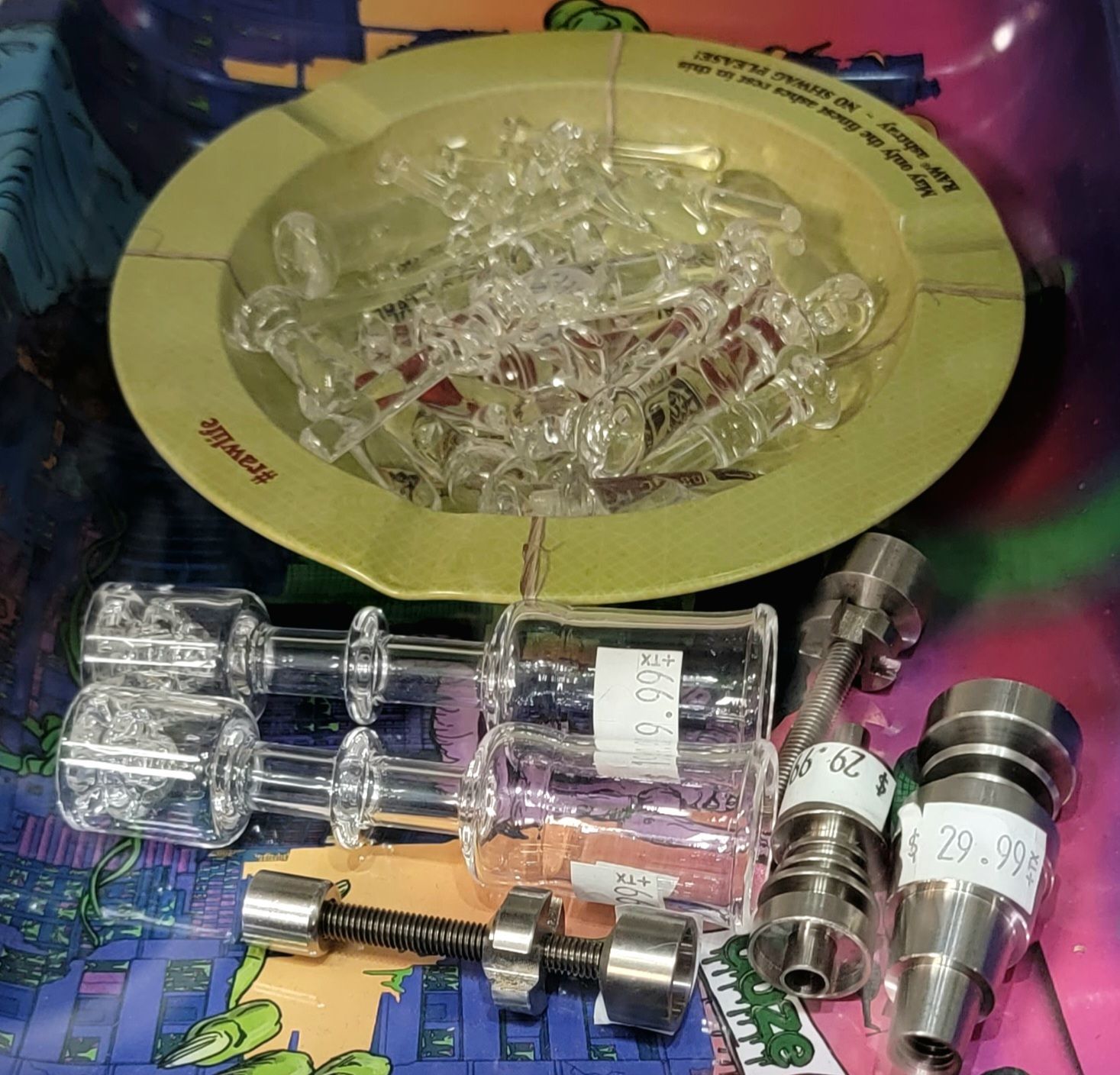 Glass and metal smoking accessories displayed on a colorful surface, including a yellow ashtray with glass tips.