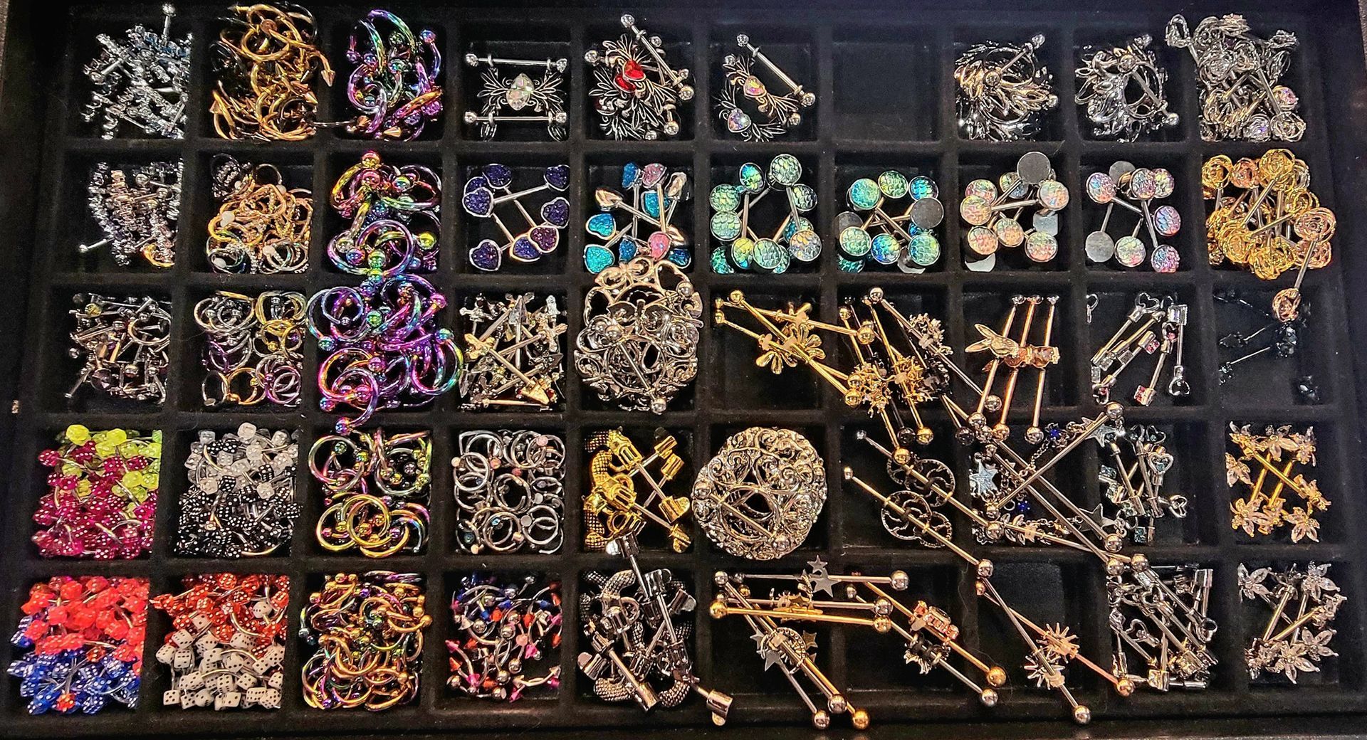 A tray of numerous colorful brooches, many with elaborate wire and jewel designs.