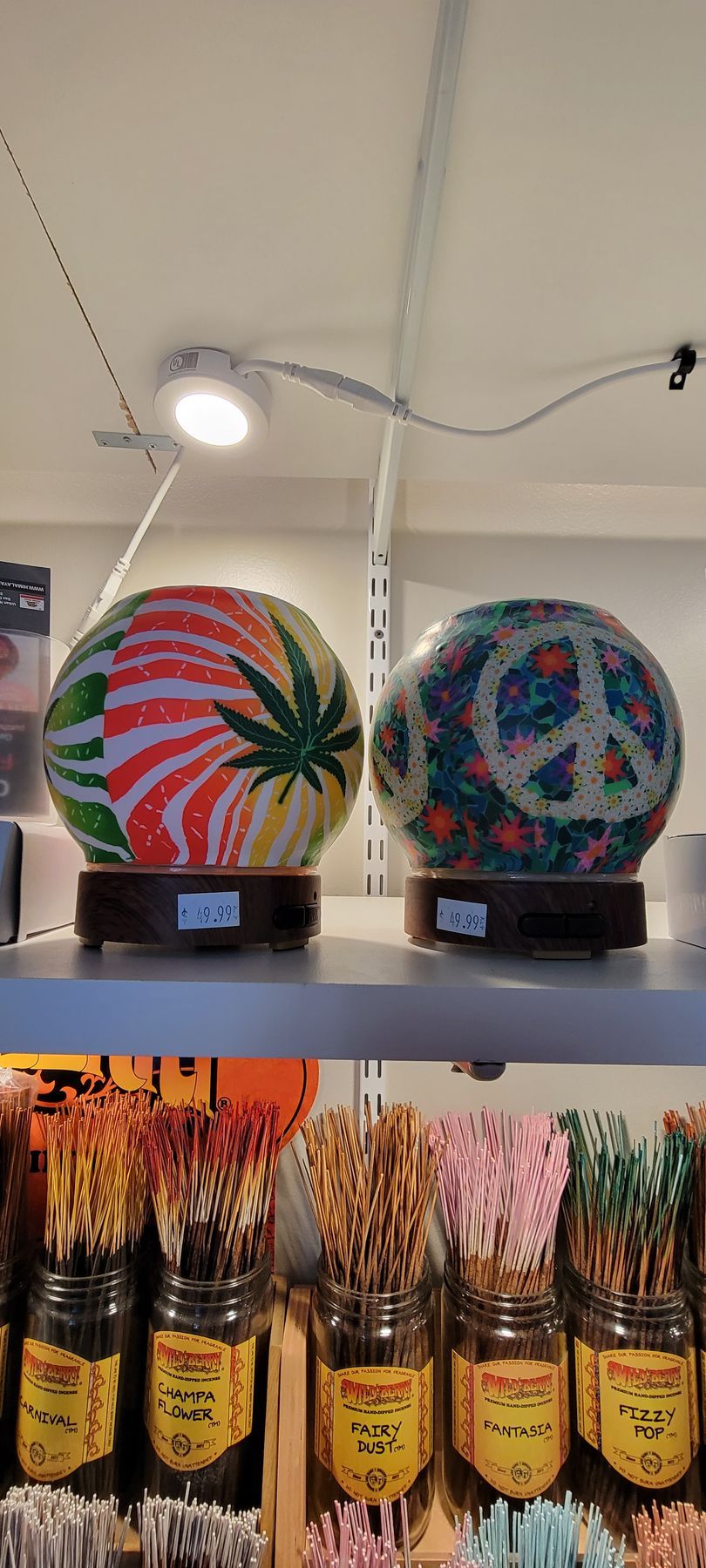 Two decorative lamps with cannabis and peace symbols, displayed on a shelf with jars of dried flowers.
