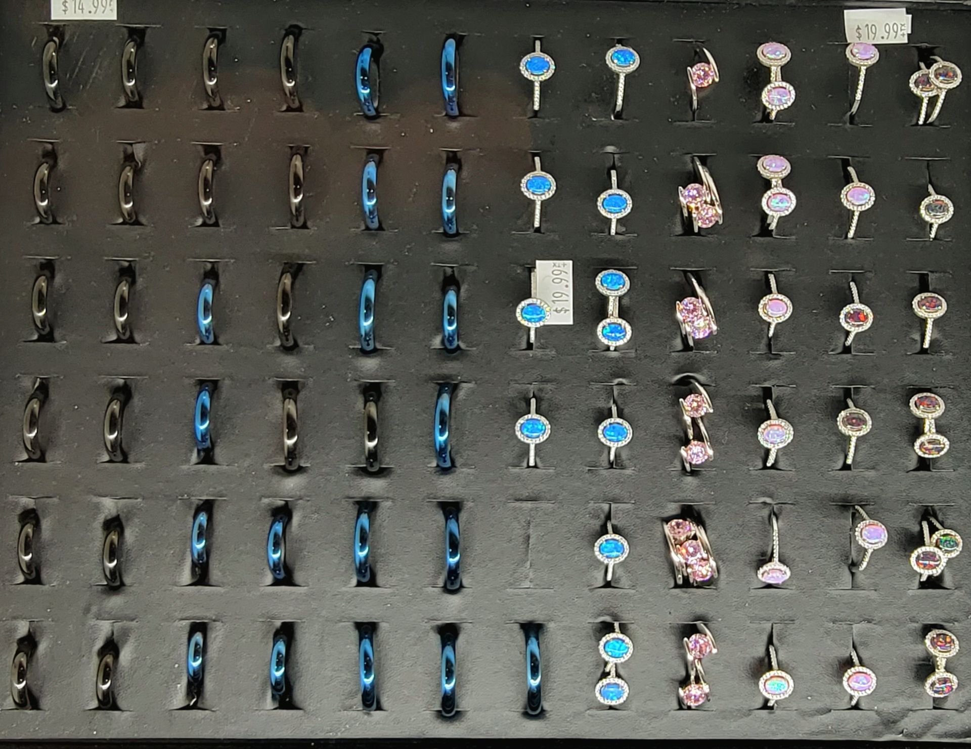 Black display case filled with rows of rings in various styles and colors, including blue and gemstones.