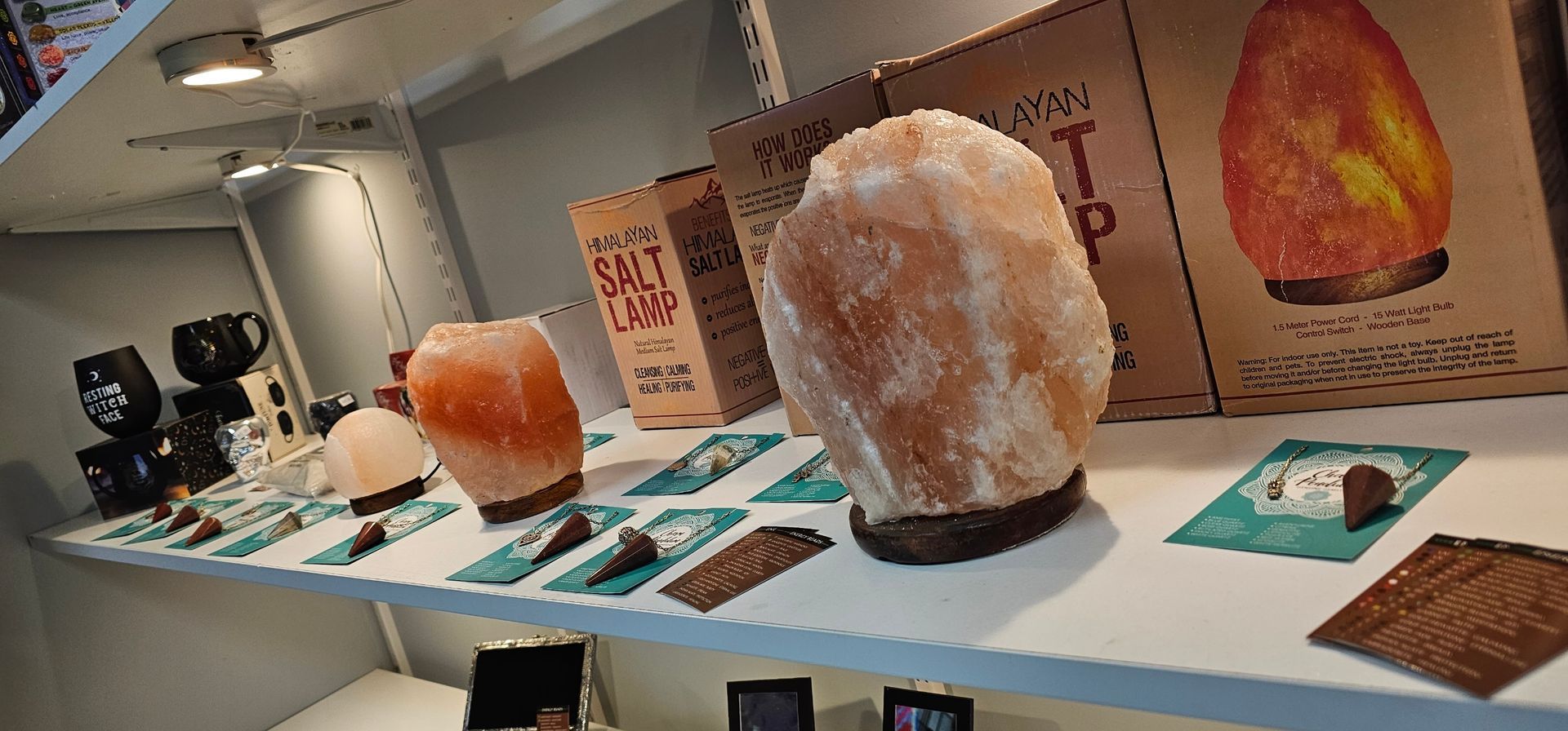 Shelves of salt lamps and products in a shop. The lamps are pink-orange. Some items are on teal cards.