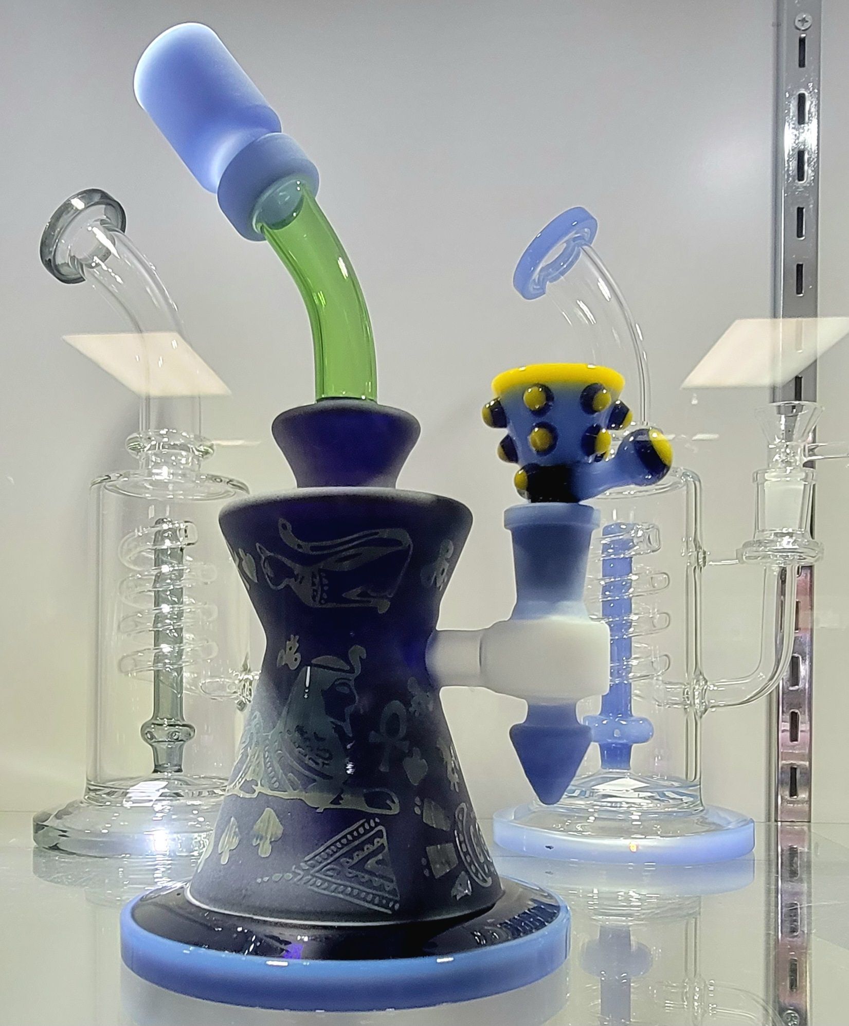 Bongs in a glass display case: blue, green, and clear glass. Each has a bowl and mouthpiece.