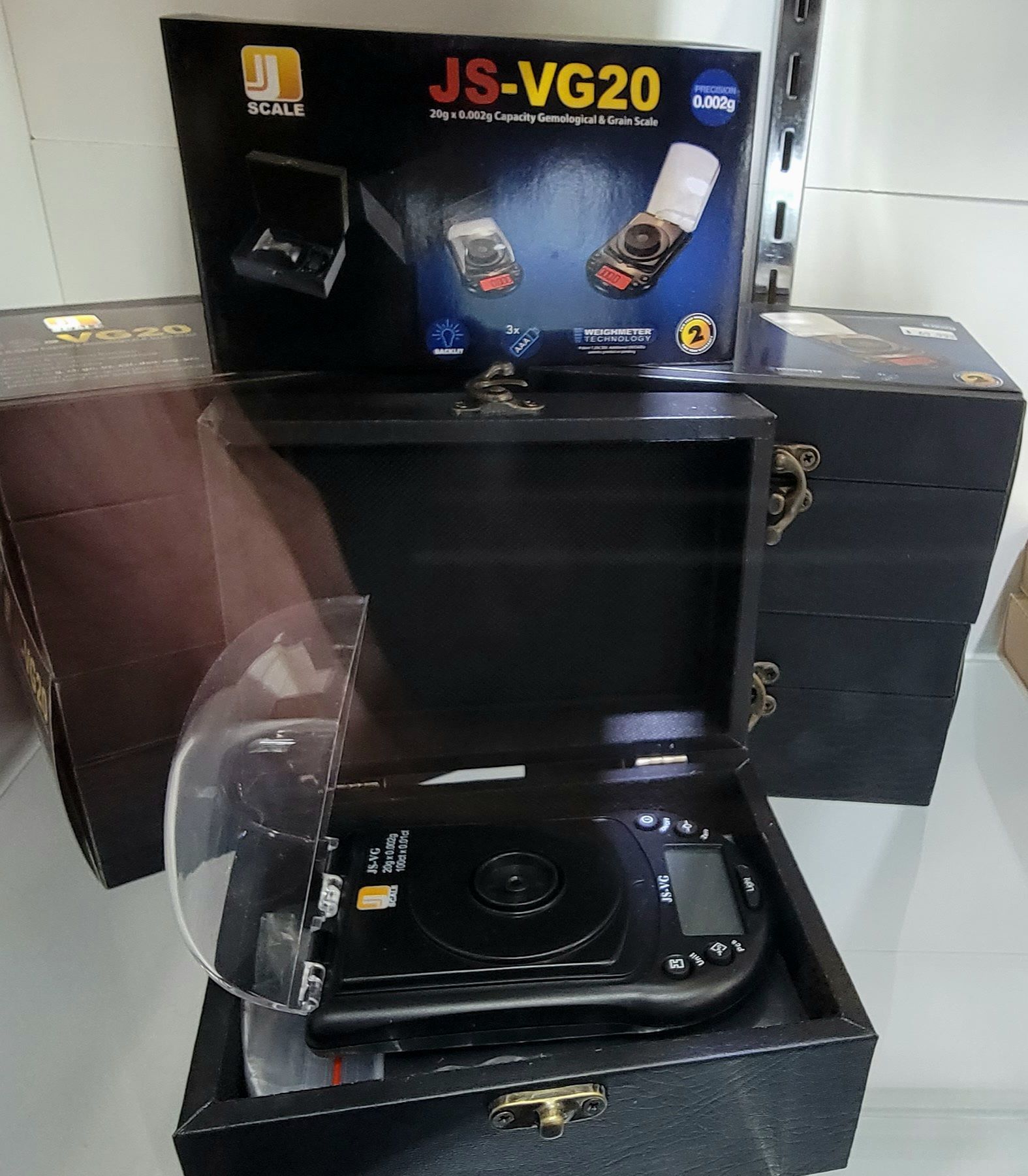 A black digital scale JS-VG20 inside a wooden box, with the product box behind it.
