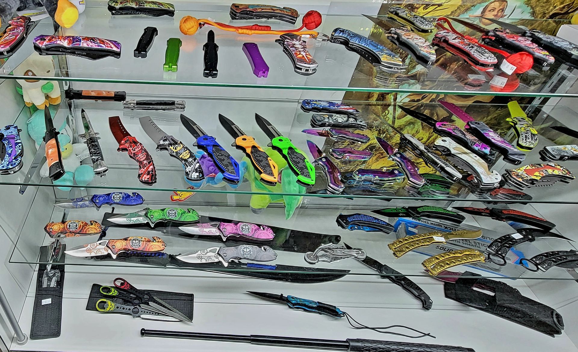 Display case filled with various colorful pocket knives, reflecting overhead lights.