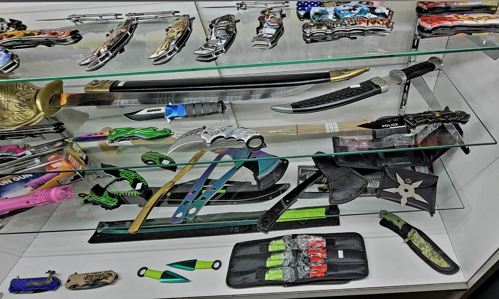 Display case of knives and axes, many with decorative handles, on shelves.