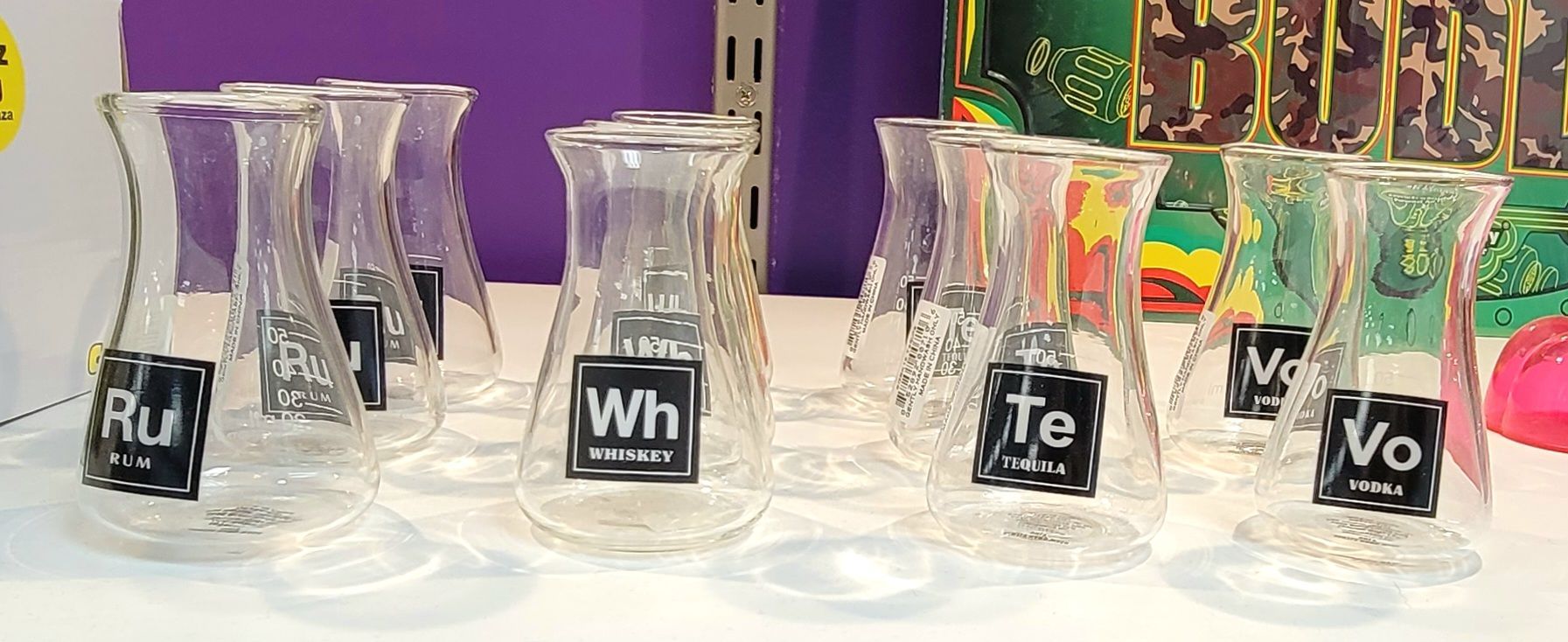 Glass beakers with periodic table element labels displayed on a white surface.