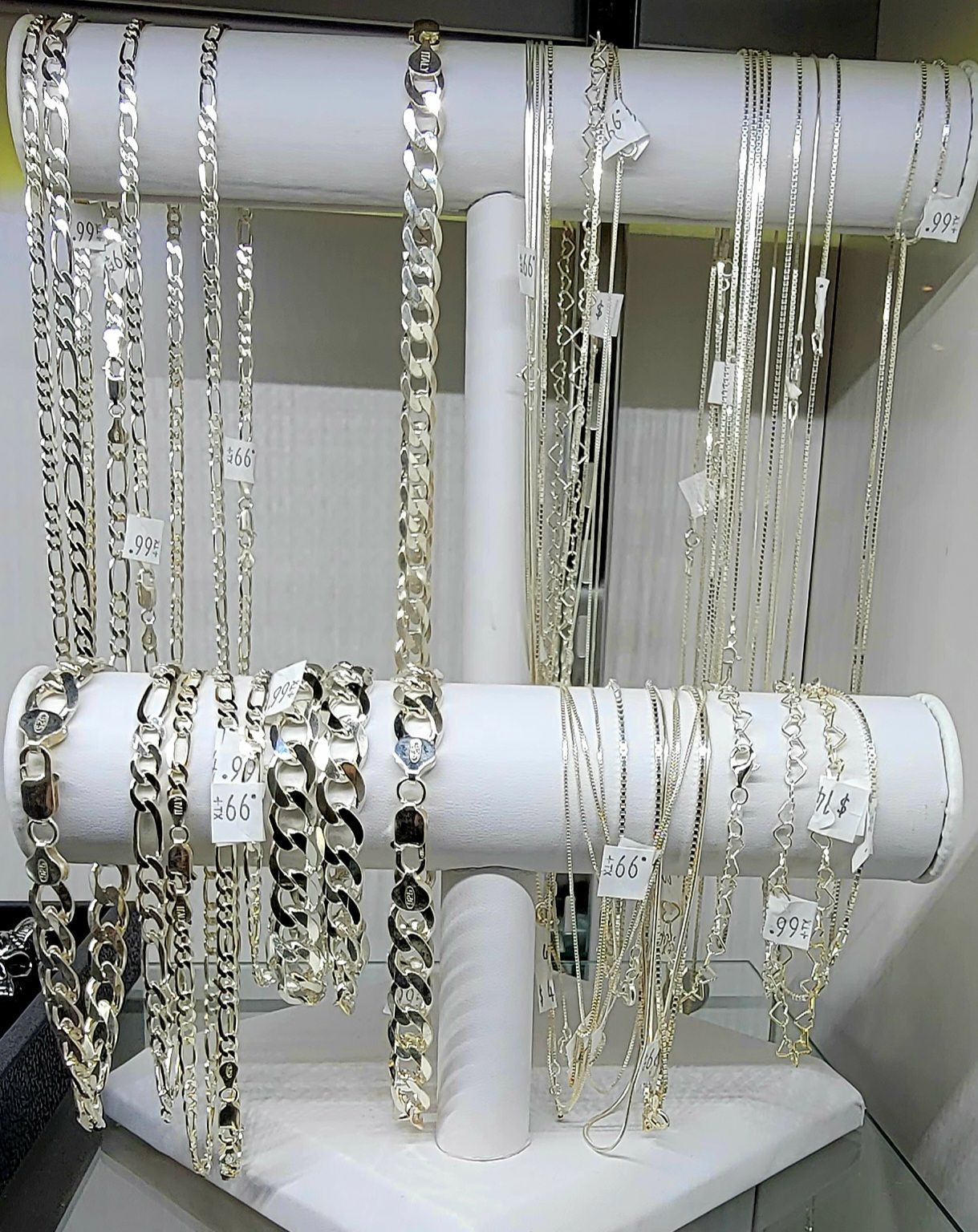 Silver necklaces and bracelets displayed on a white jewelry stand.