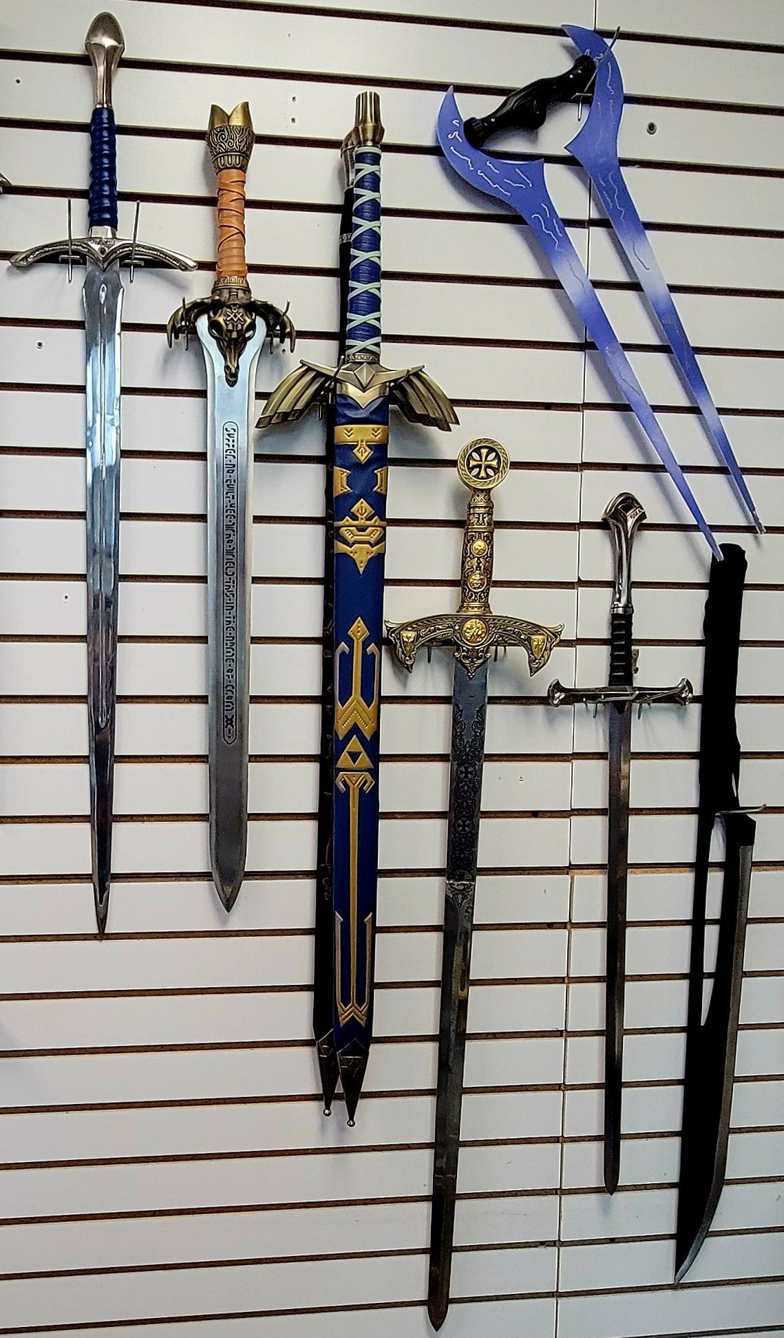Swords displayed on a striped wall; various designs, including a blue energy sword and a sword with a blue sheath.