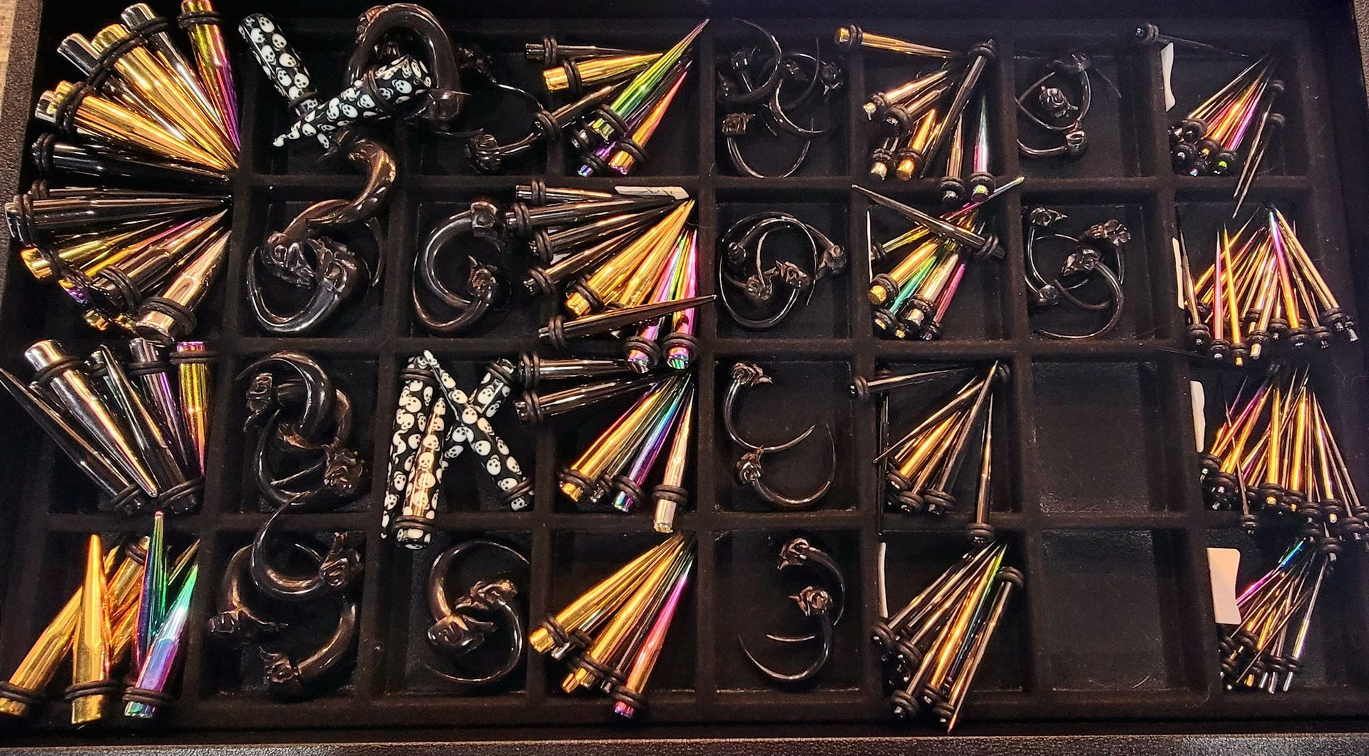 A tray of iridescent butterfly knives, with various shapes and blade patterns in a black display.