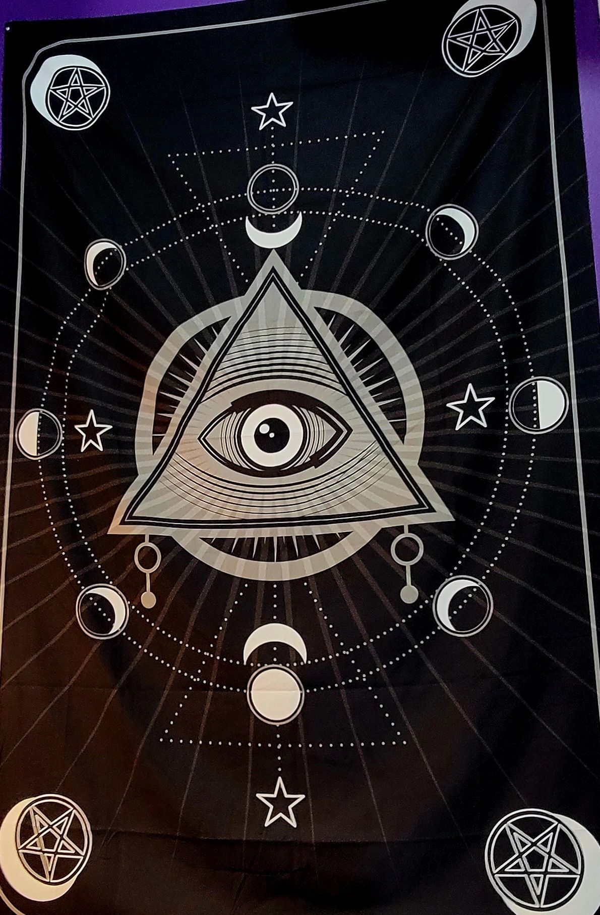 Black tapestry with an eye in a triangle, surrounded by moons, stars, and geometric shapes.