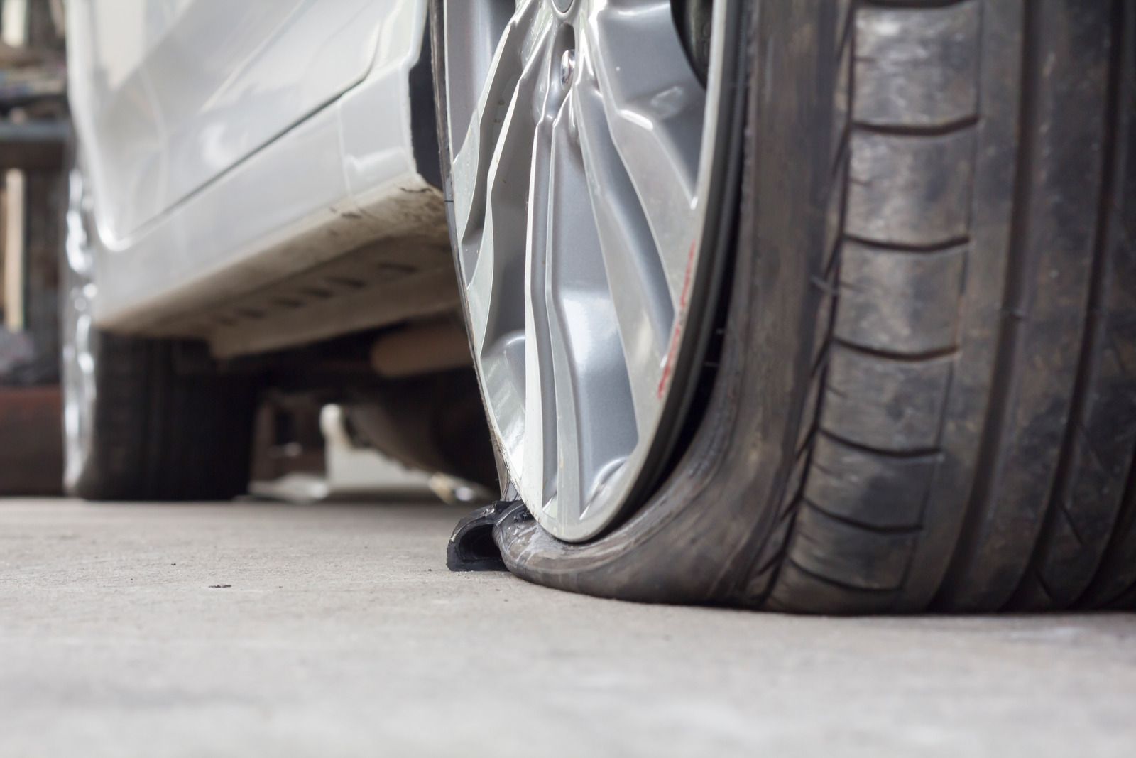 A flat car tire on a light-colored car. The tire is deflated and resting on the concrete.