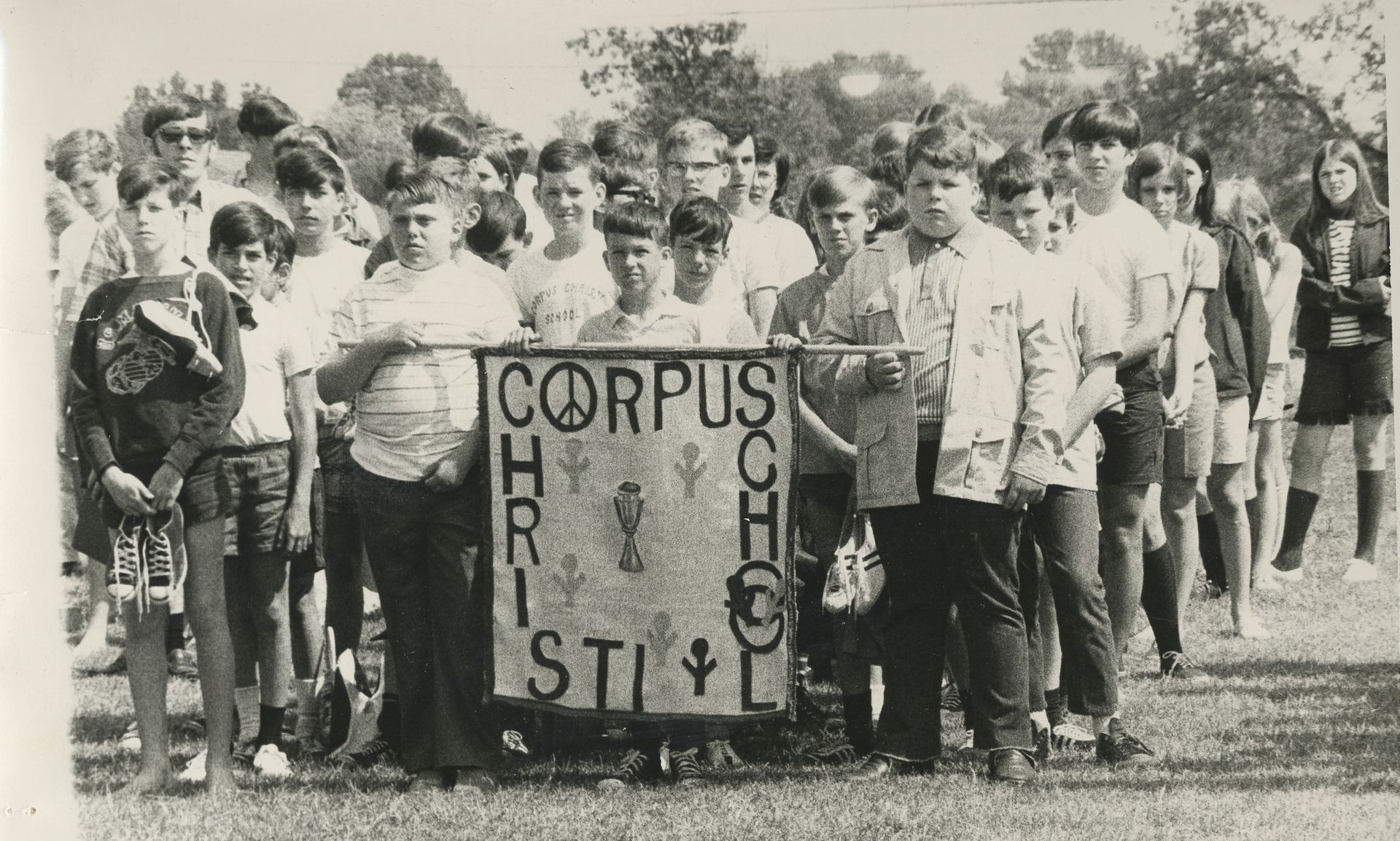 Two smiling boys with arms around each other in a park. One wears a track cleats around neck, the other a striped shirt.