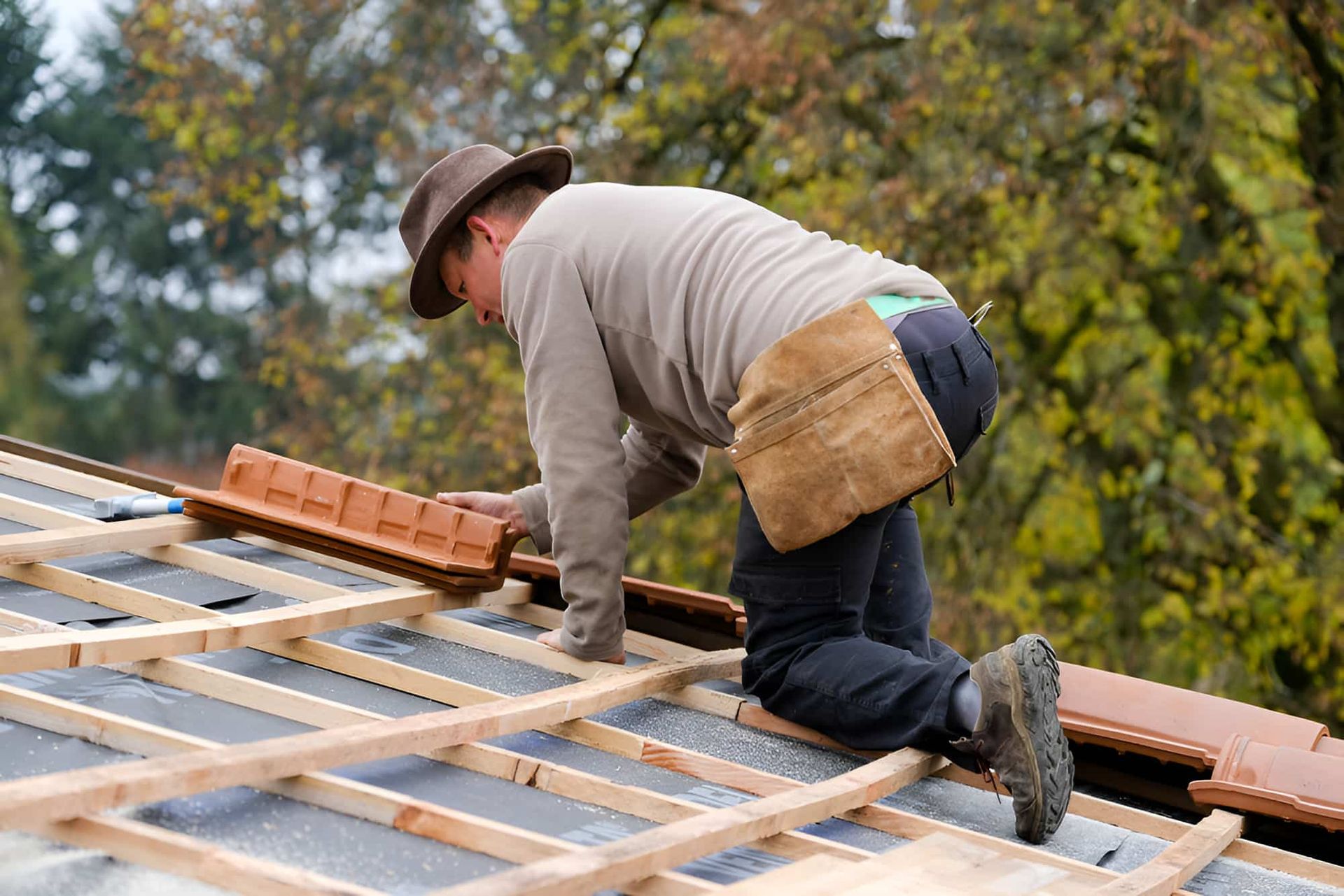 A Man Is Kneeling On Top Of A Wooden Roof — QB Roof Tiling Services In Maroochydore, QLD