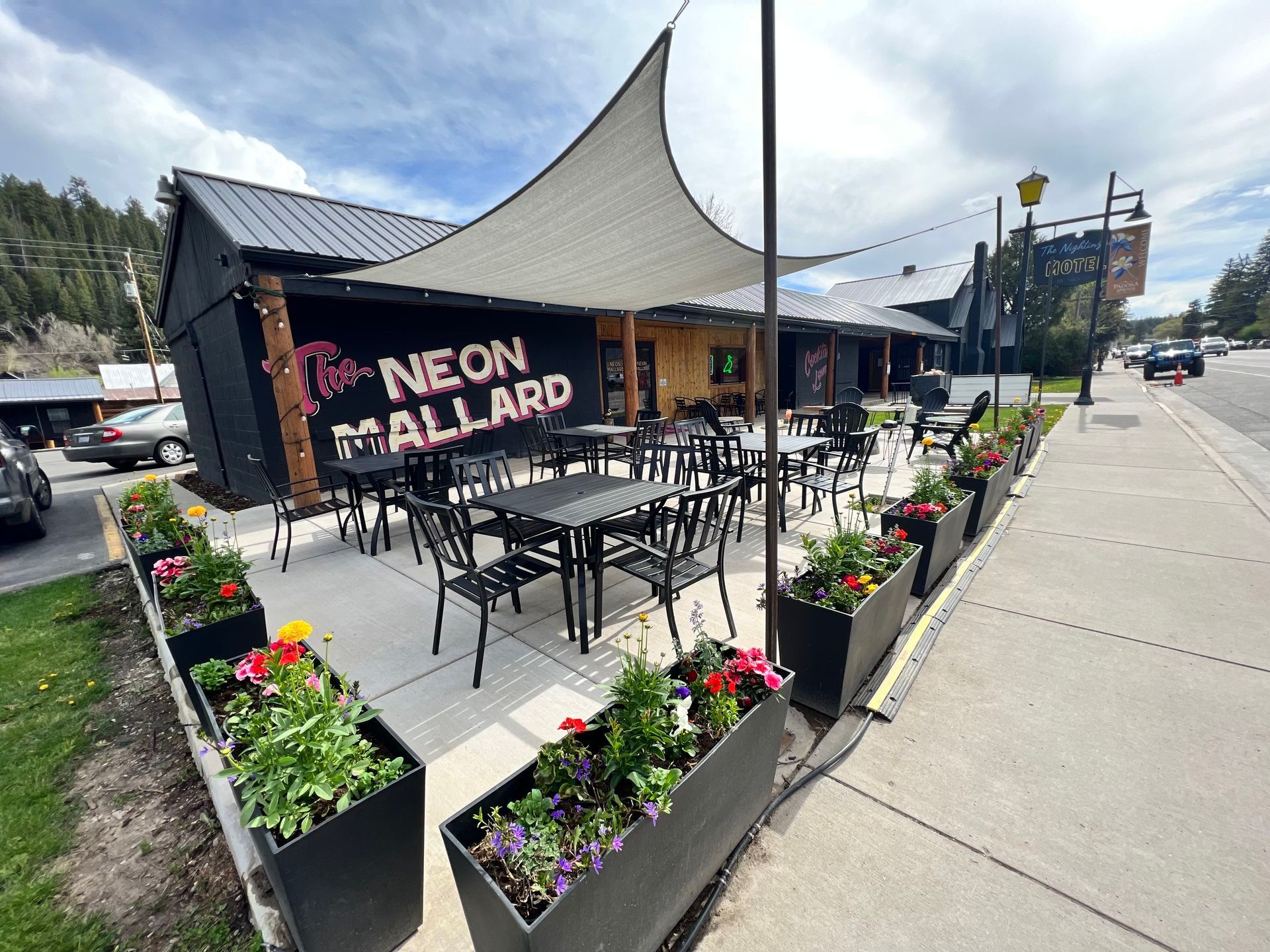 Exterior view of Neon Mallard restaurant with outdoor seating and flower boxes.