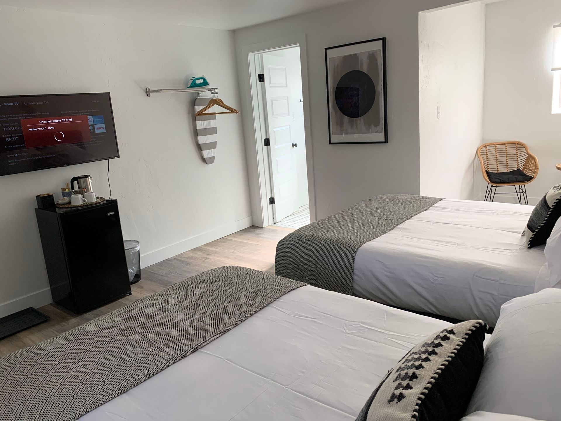 Hotel room with two beds, TV, and mini-fridge. Neutral colors with a door leading to a bathroom.