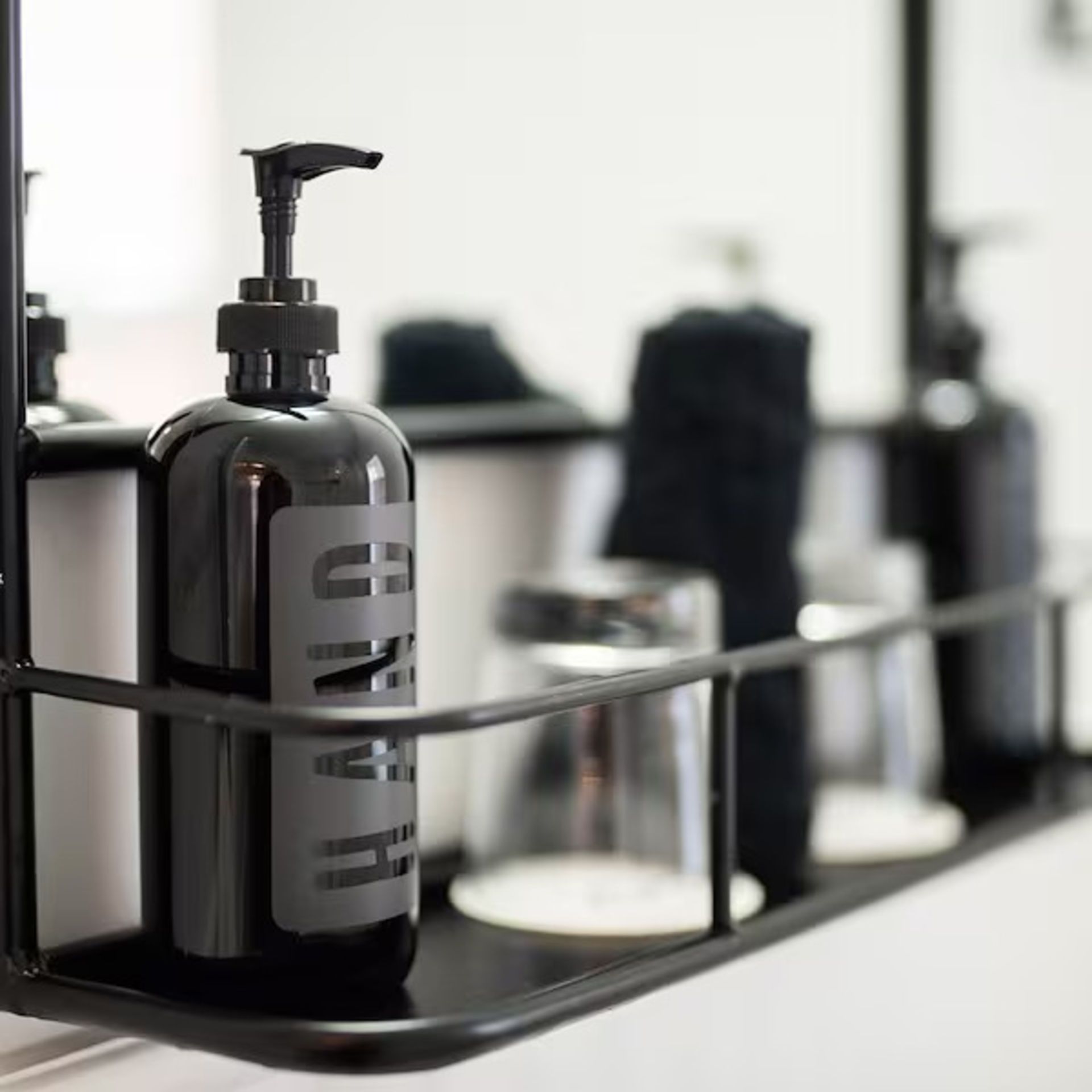 Black hand soap dispenser in a wire rack, with glasses and other bathroom items.