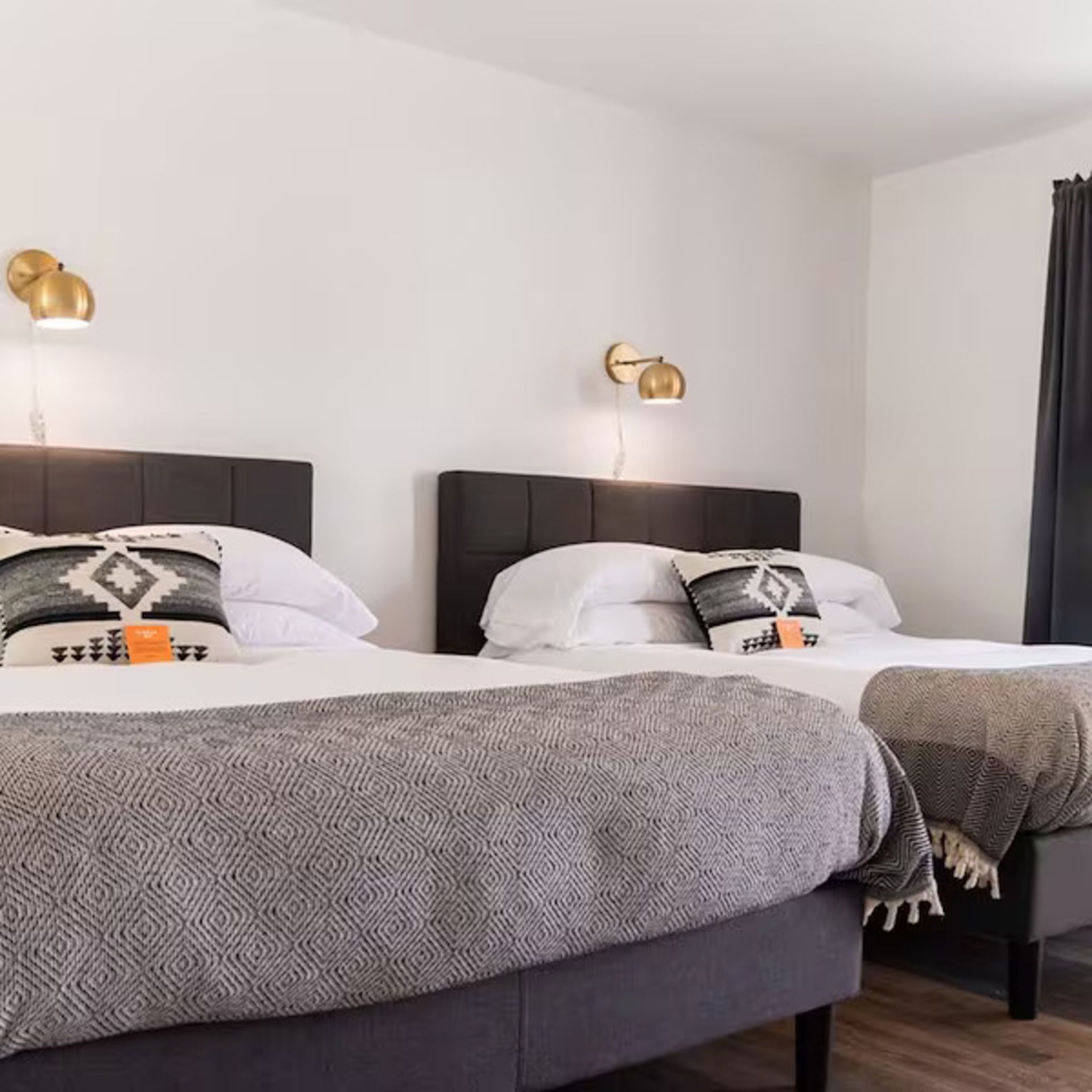 Two beds in a room with white walls, gold sconces, and gray bedding.