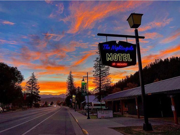 Sunset over The Nightgate Motel sign and a small town road, with mountains and trees.