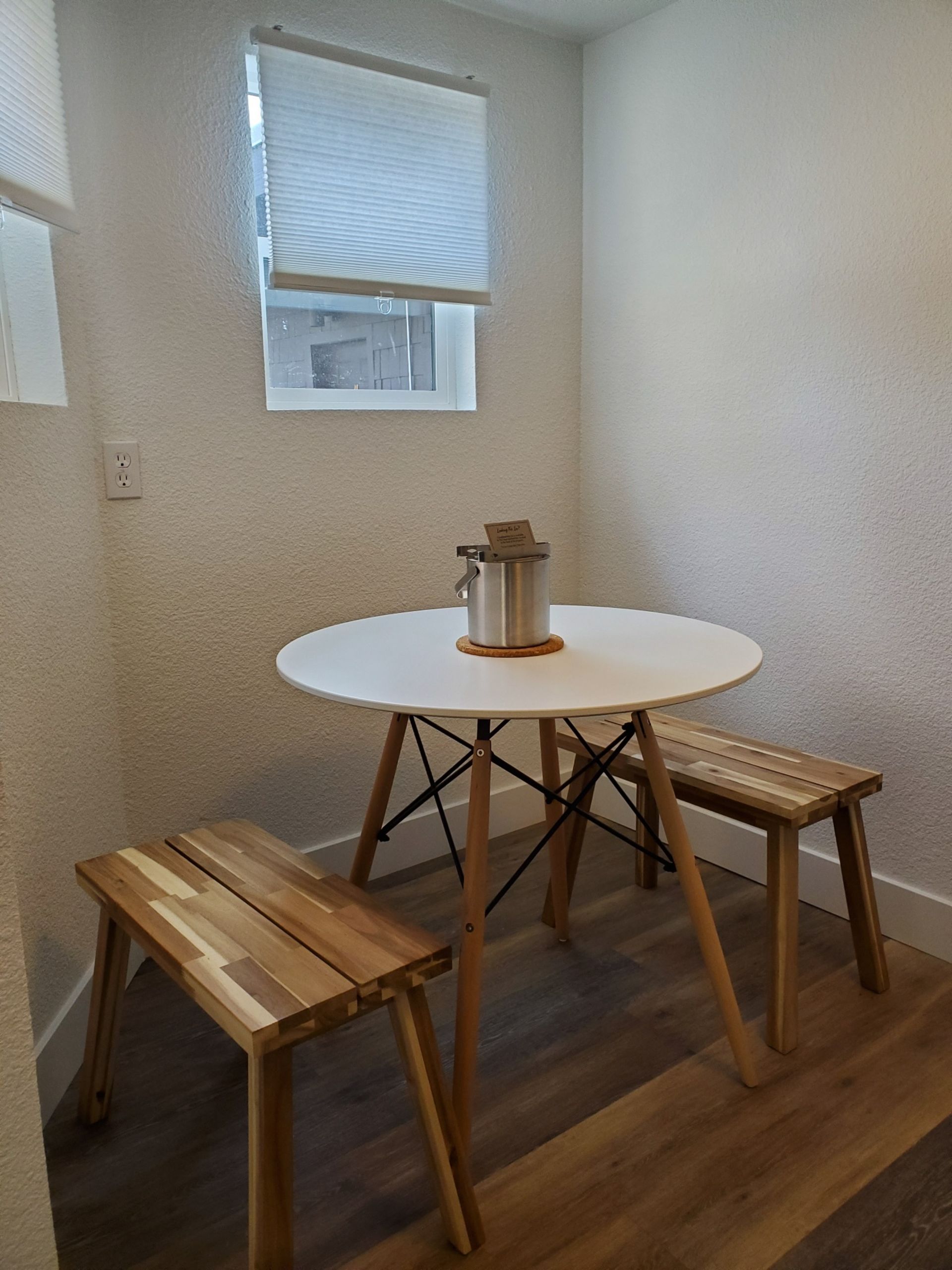 Small dining area with white table, two wooden benches, and a window with a shade.
