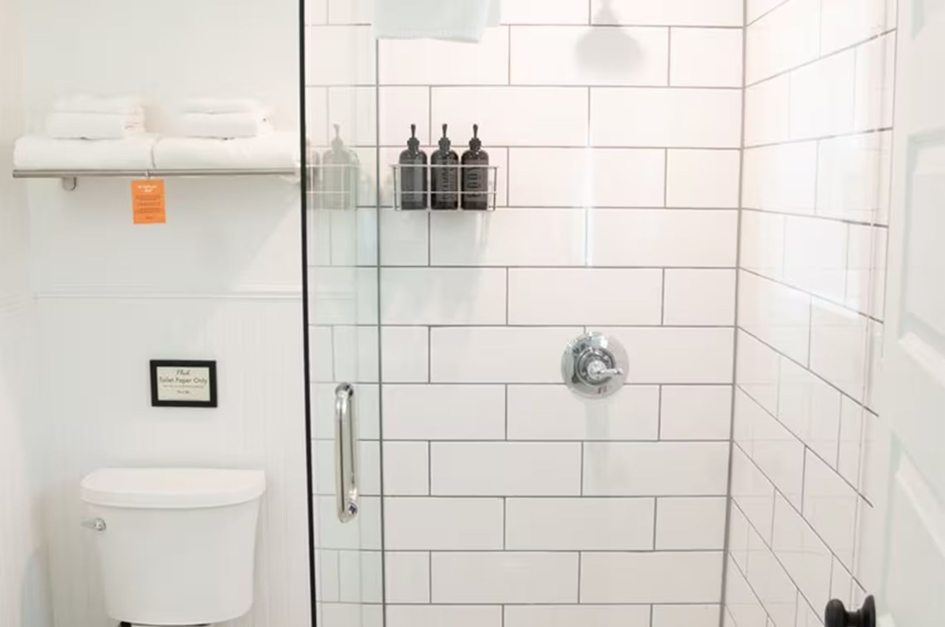 Bright, white bathroom with subway tile shower, toilet, and shelf with towels.