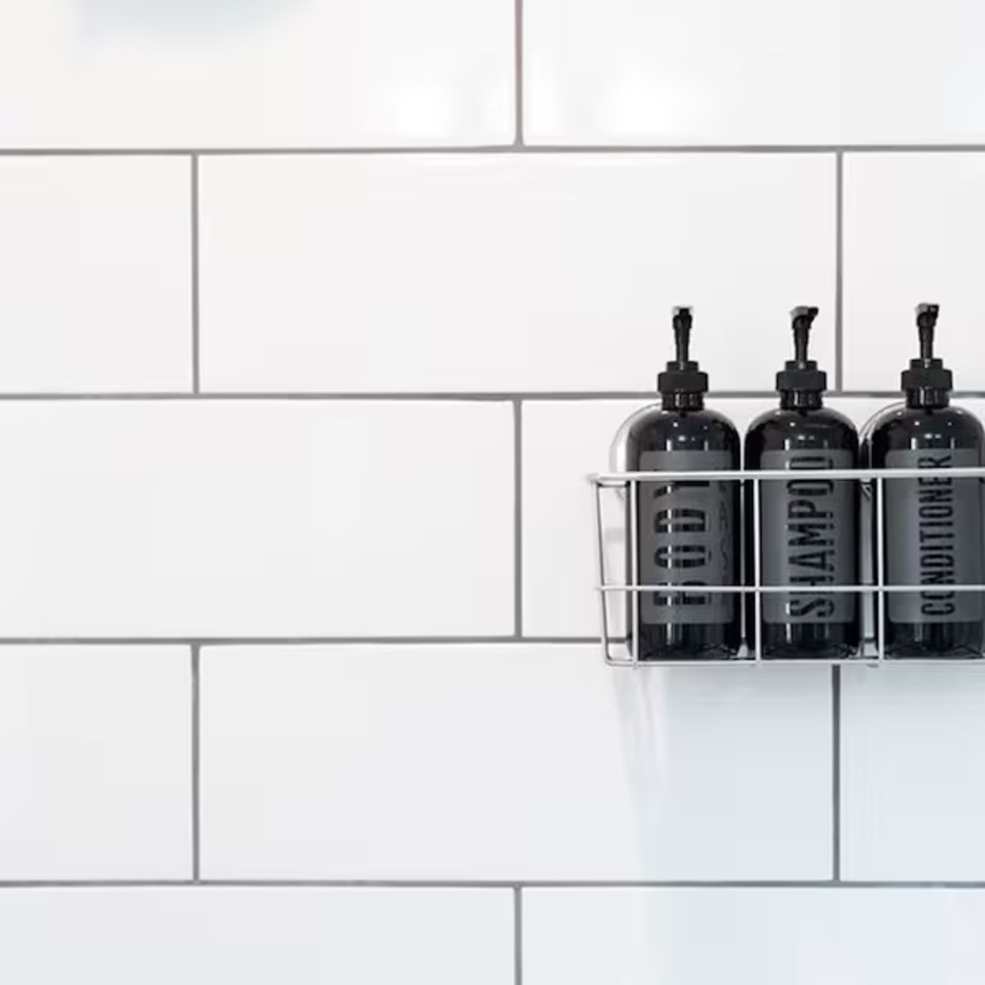 Black shampoo bottles in a metal rack on white subway tile wall.